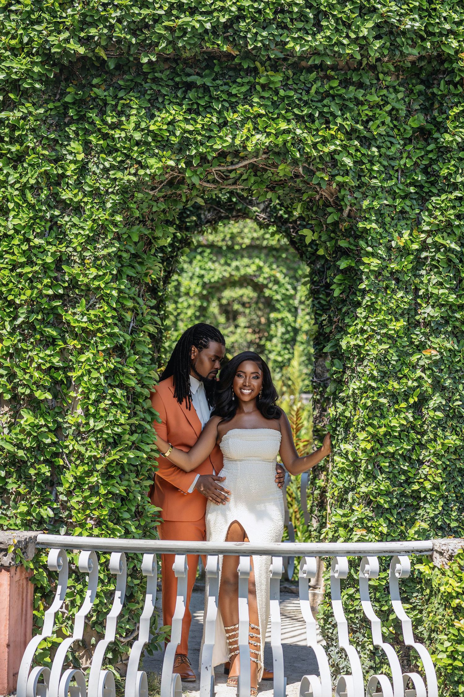 Romantic couple embracing under ivy-covered arch tunnel on white balcony during engagement session.