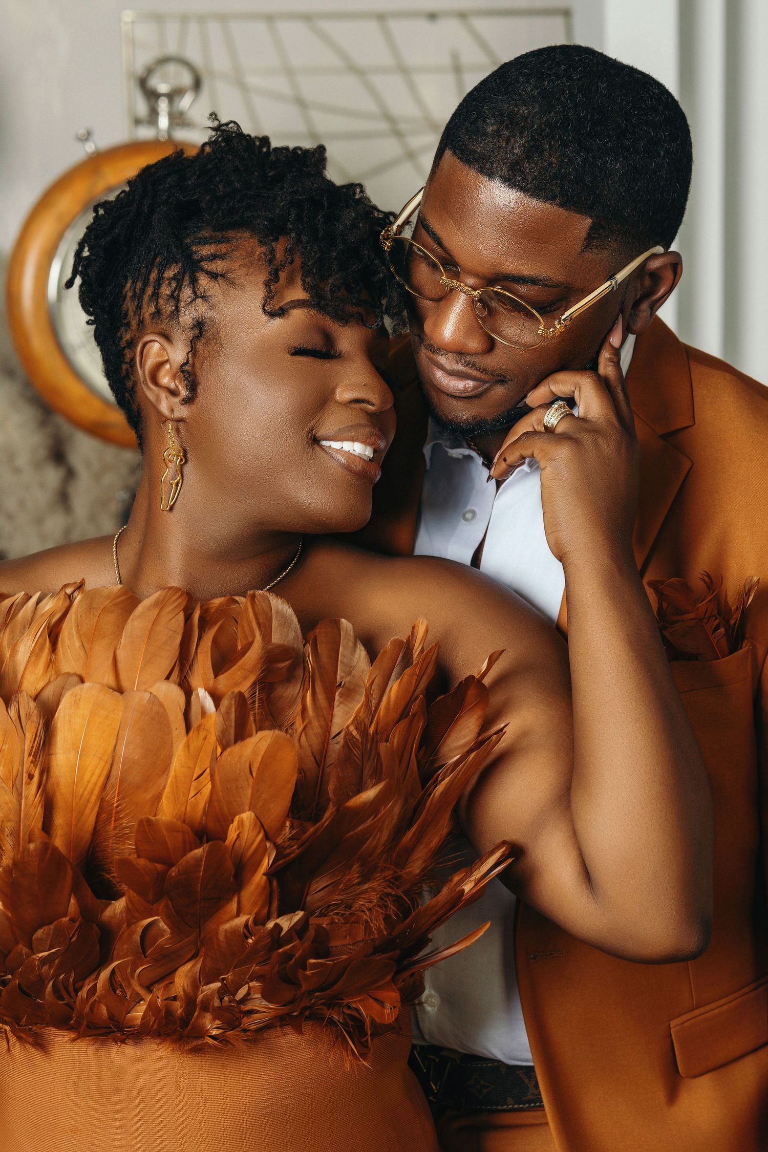 Close romantic moment between a smiling woman in feathered orange dress and man in orange suit with gold glasses.