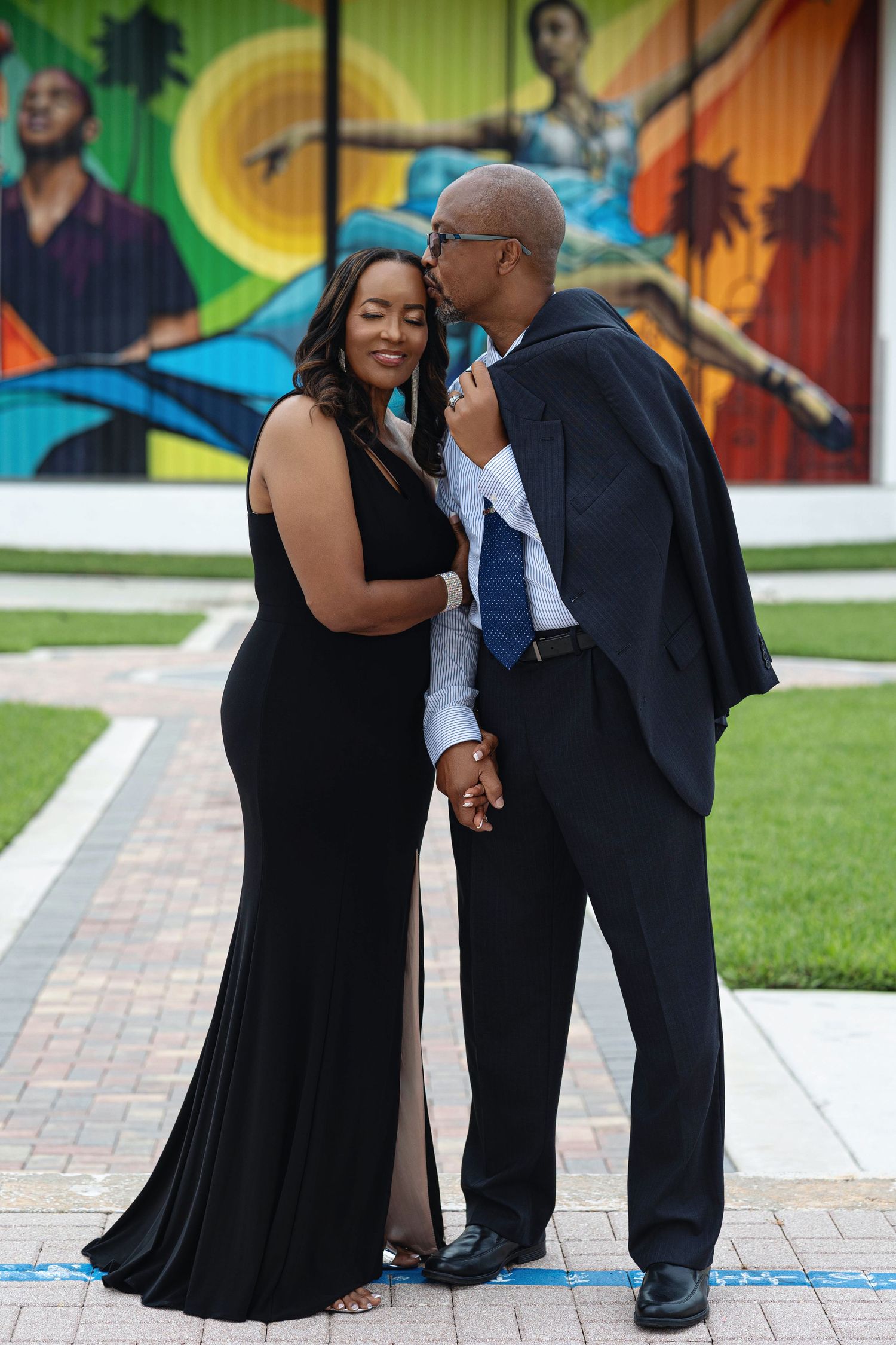 Romantic engaged couple sharing a tender kiss outdoors in front of a vibrant colorful mural backdrop.