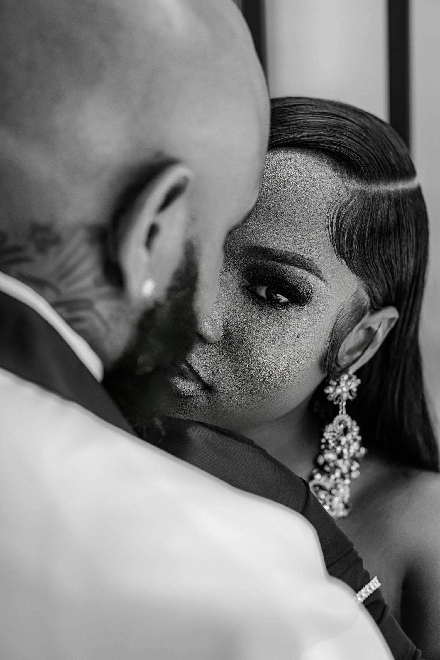 Black and white intimate portrait of bride and groom touching foreheads, bride wearing elegant chandelier earrings.
