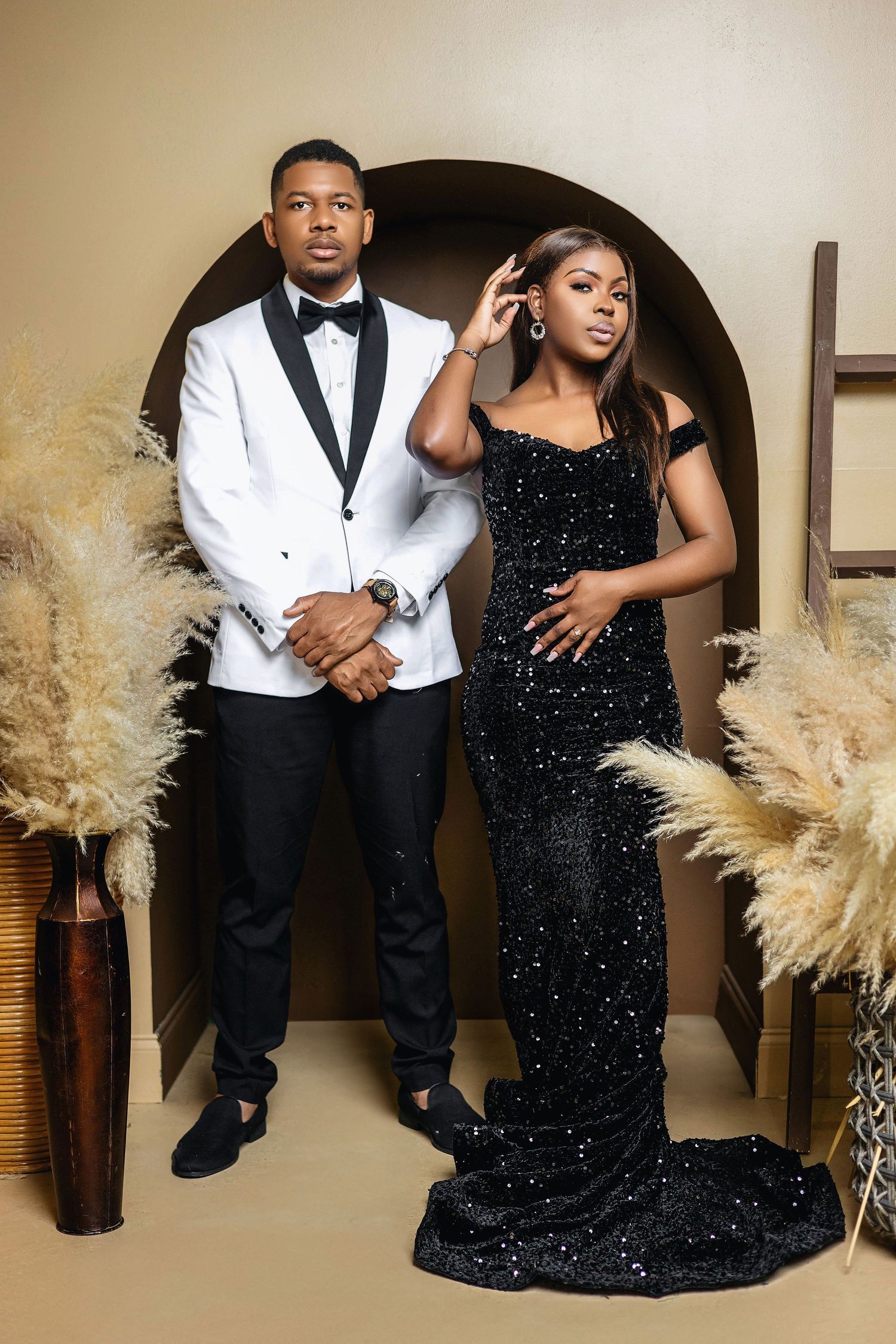 Stylish couple in black and white formal wear posing in studio with pampas grass decor.