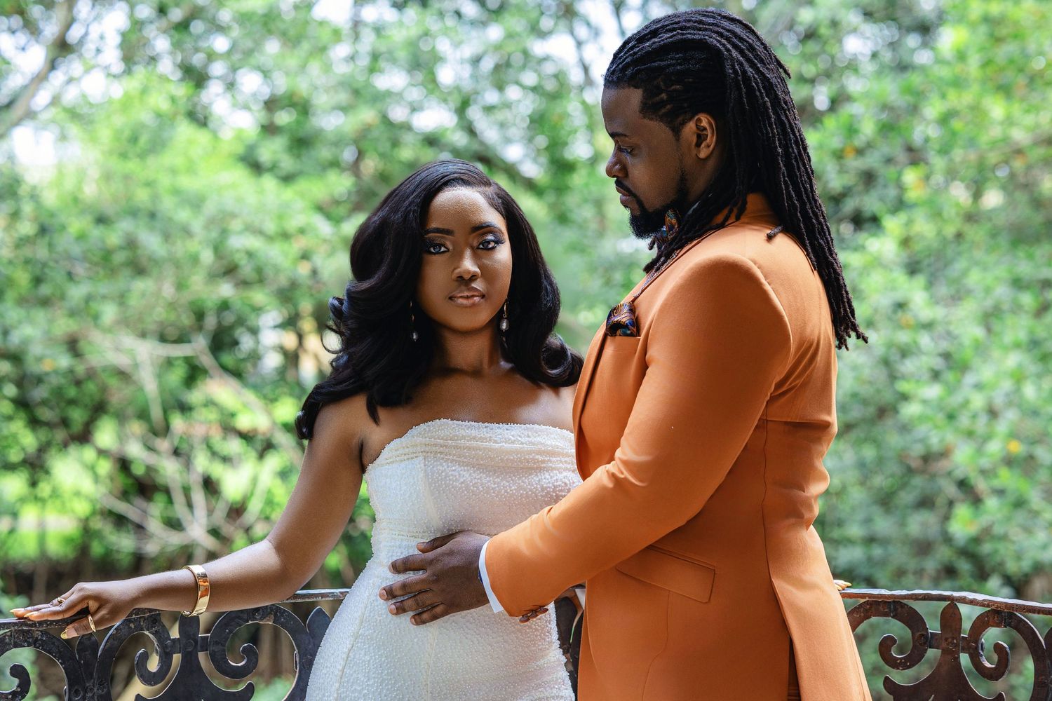 Bride in white strapless gown and groom in orange suit share a romantic moment.