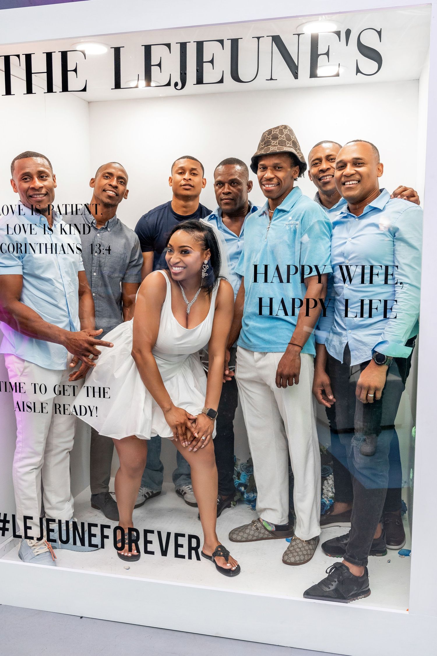 Bride in white dress surrounded by six men posing inside The Lejeune's wedding celebration photo booth.