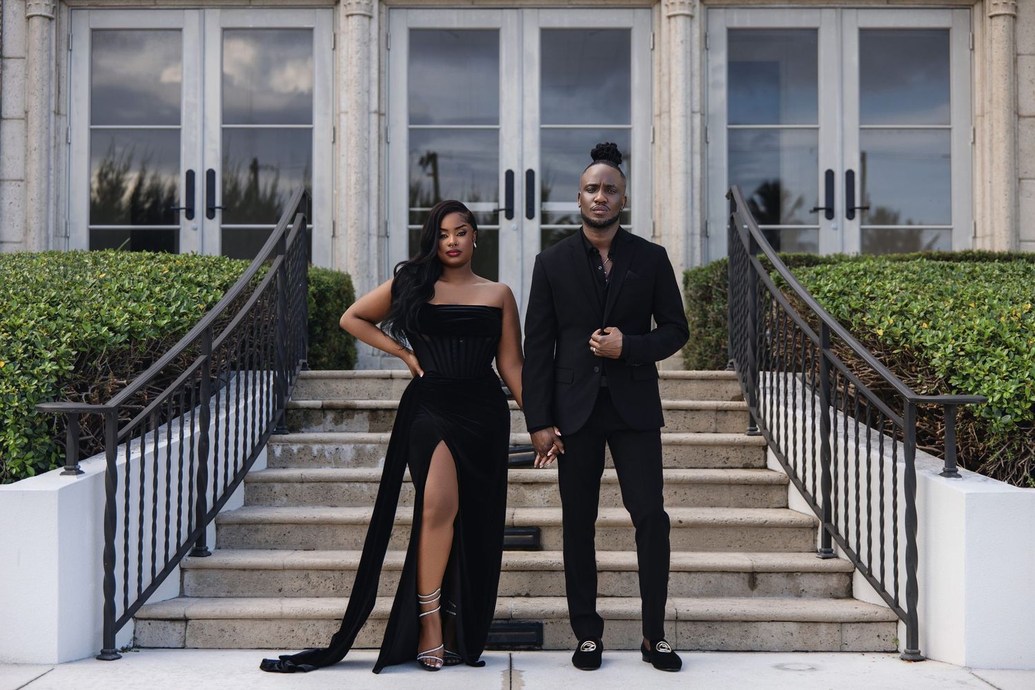 Elegant couple in matching black formal attire posing on grand exterior staircase.
