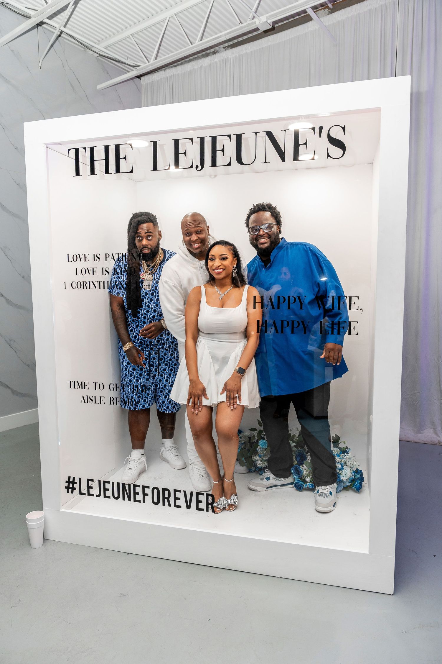 Two men and a woman in white smile together inside The Lejeunes LejeuneForever decorative photo frame backdrop.