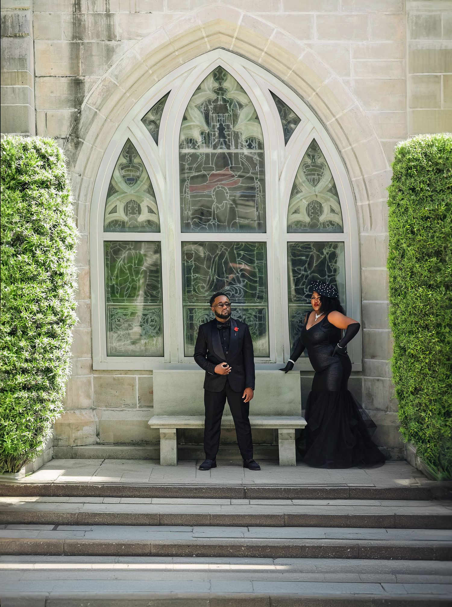 Elegant couple in matching black formal attire posing before a Gothic stone church window.