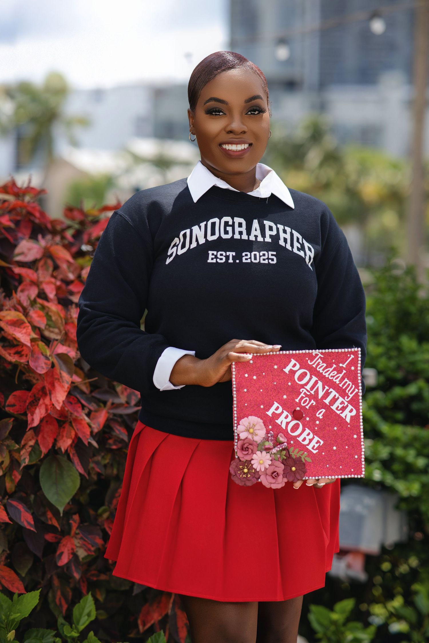 Proud Black woman in Sonographer Est. 2025 sweatshirt holding red graduation cap decorated with Pointer for a Probe.