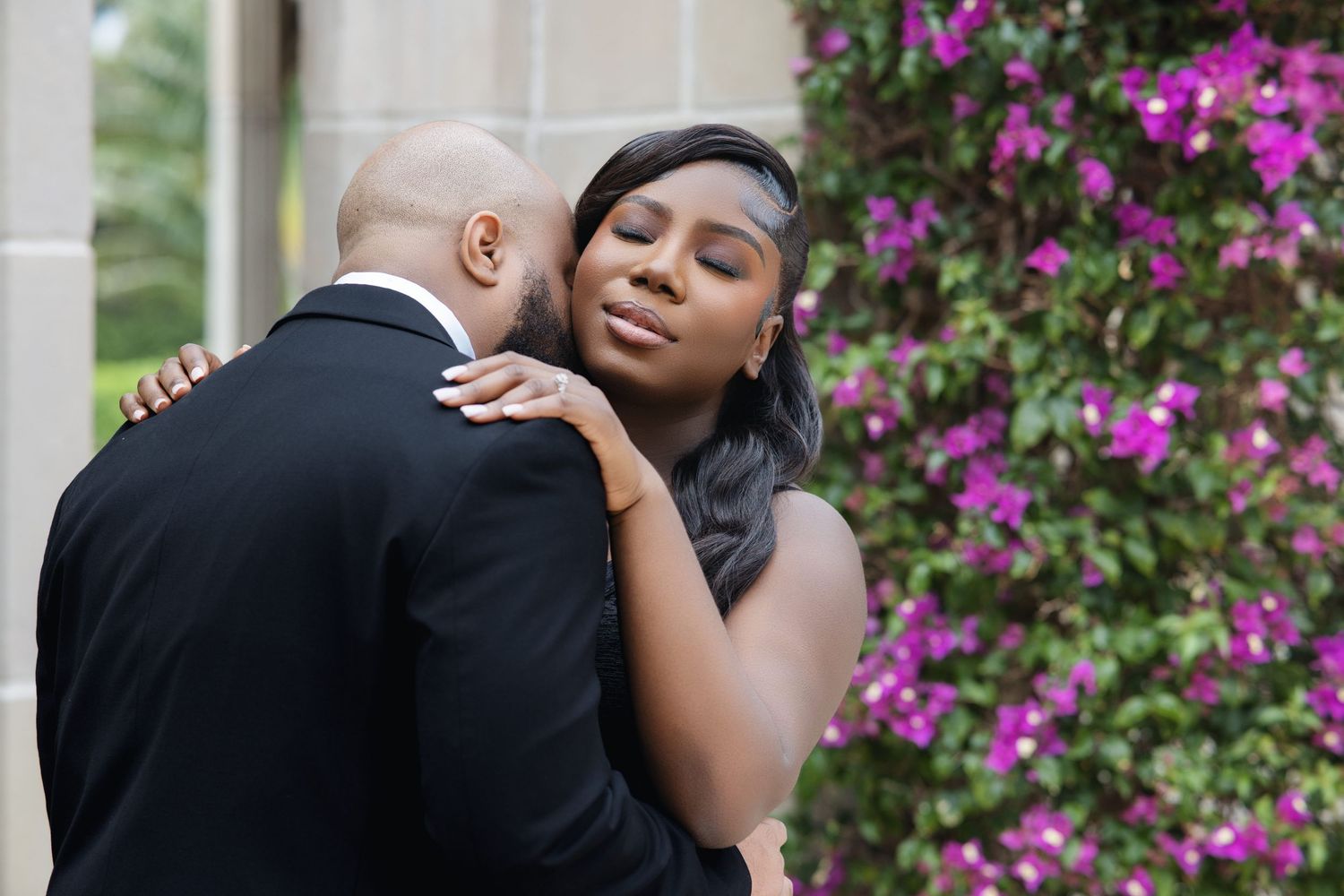 Black couple in a romantic embrace near vibrant purple bougainvillea during outdoor shoot.