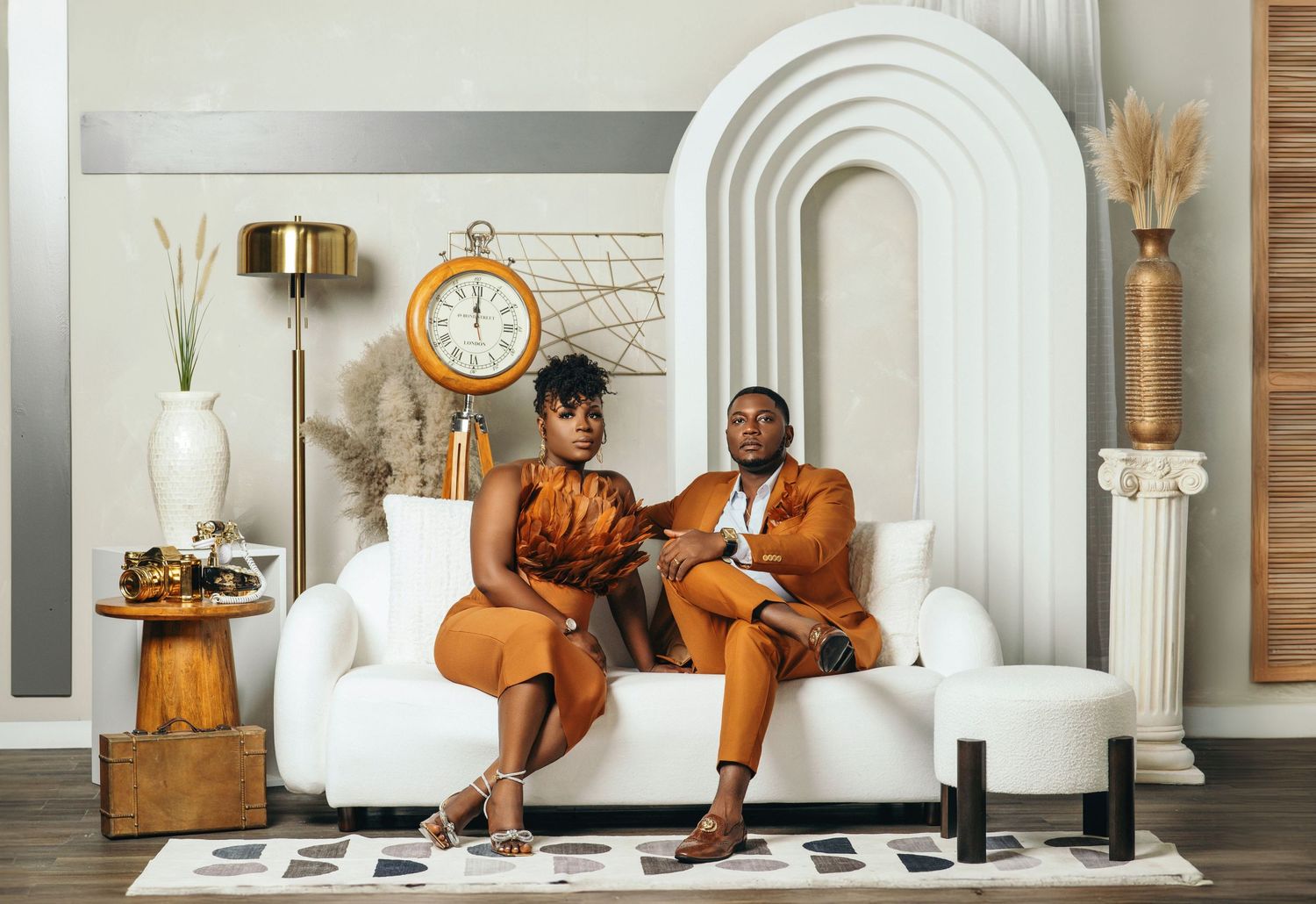 Couple in matching burnt orange ensembles relaxing on a white sofa in a luxe interior.