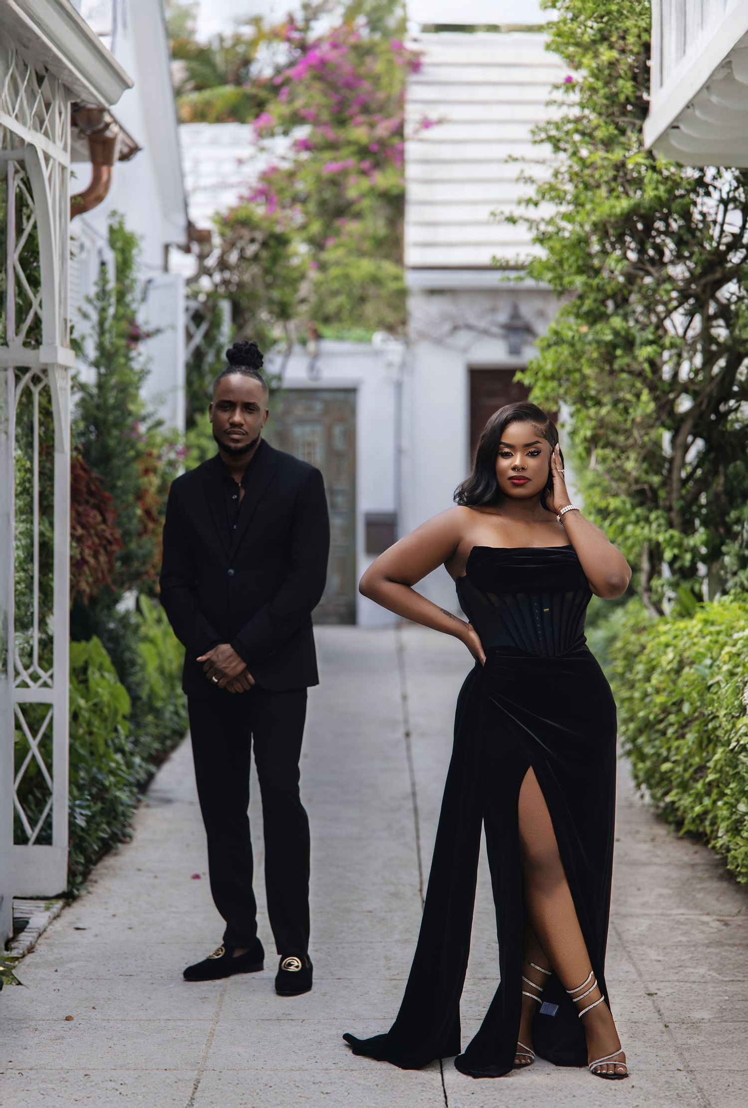 Couple in matching black formal attire posing in garden pathway.