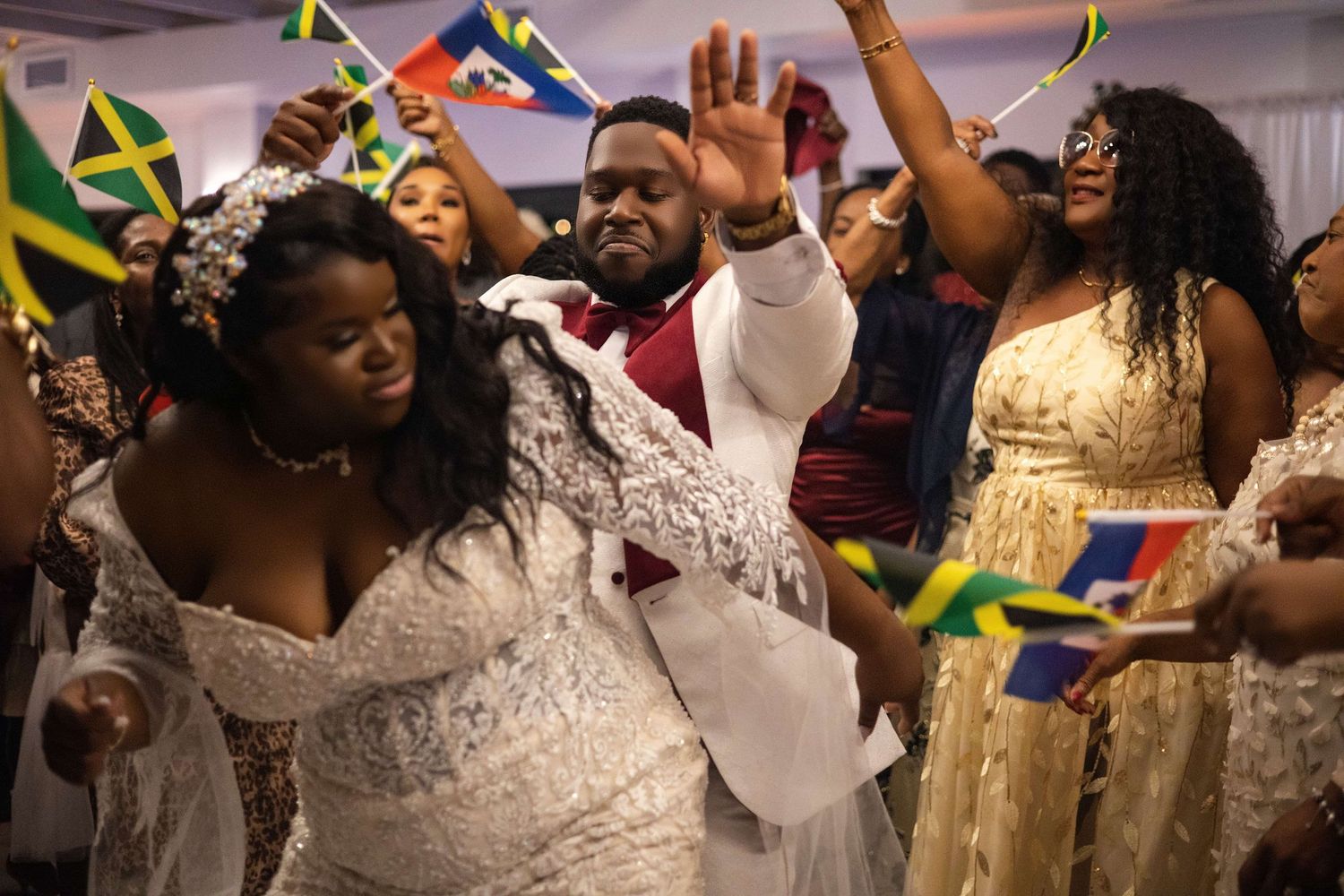 Bride and groom celebrate with guests waving Jamaican flags at a vibrant multicultural wedding reception.