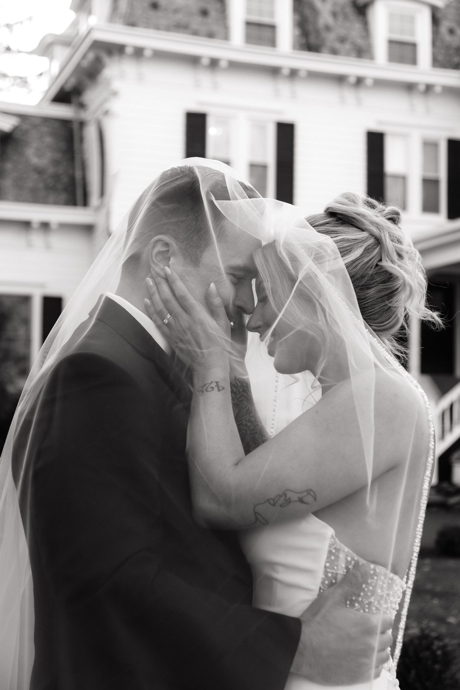 Black and white photo of bride and groom sharing an intimate moment under a bridal veil.