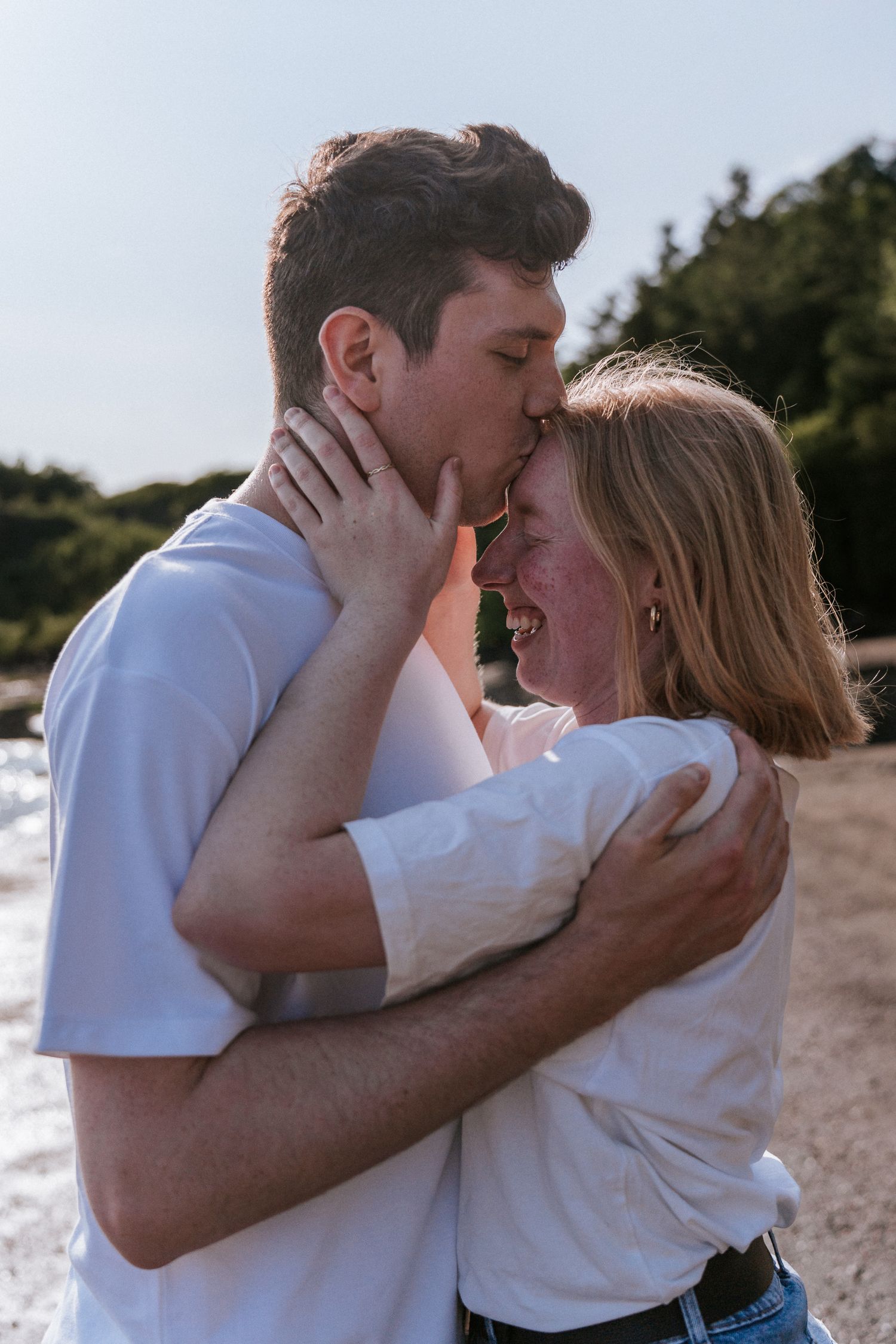 Un couple d'amoureux en chemises blanches s'échange un tendre baiser au bord de l'eau, par un après-midi ensoleillé.