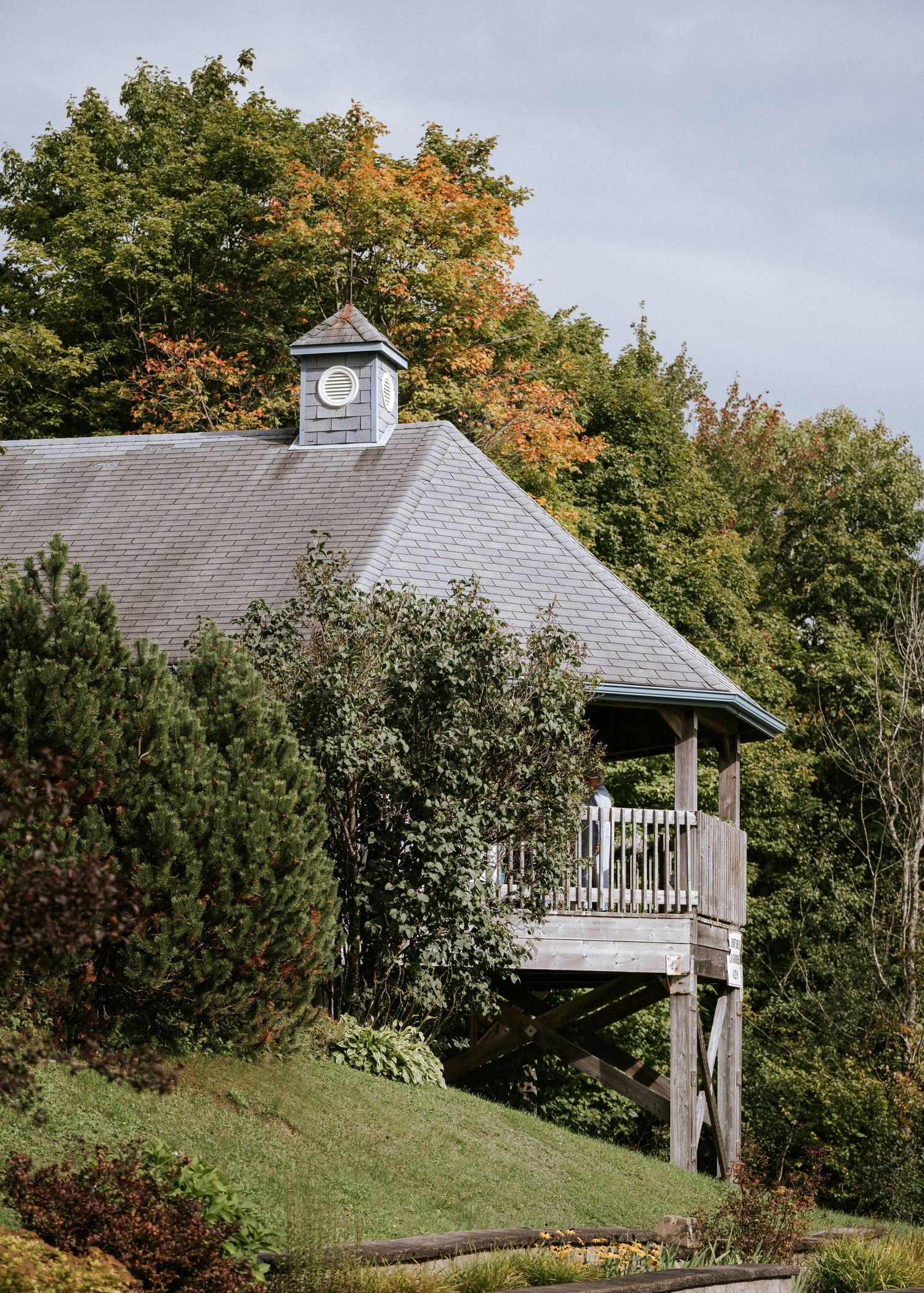 Charmant gazebo en bois avec coupole d'horloge, niché parmi les arbres d'automne sur une colline.