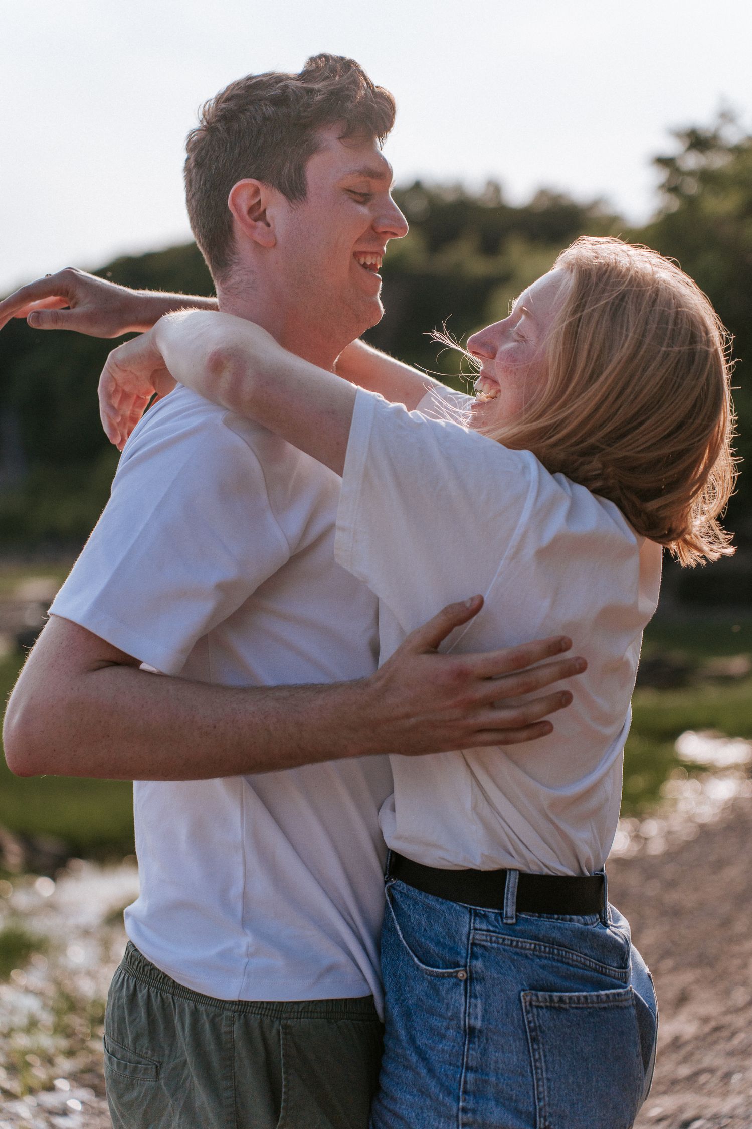 Un couple heureux en t-shirts blancs s'enlaçant et riant ensemble en plein air, pendant l'heure dorée.