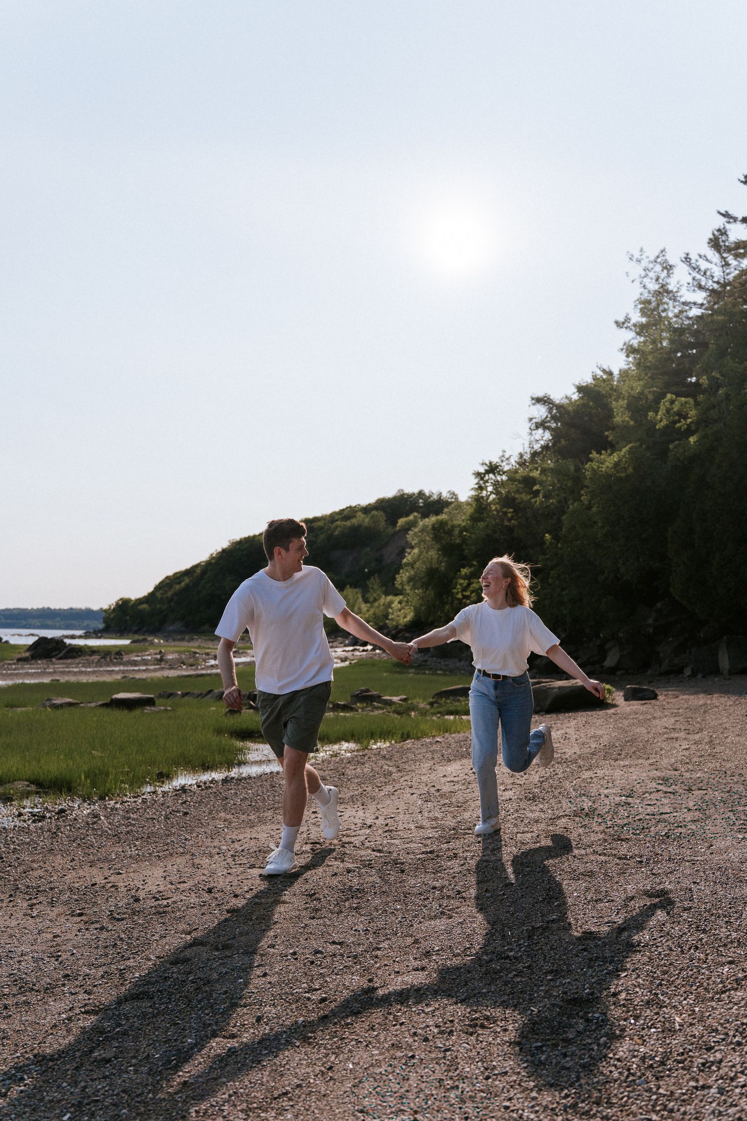 Un couple en tenue décontractée se tient la main en courant joyeusement le long d'un sentier sur une plage rocheuse.