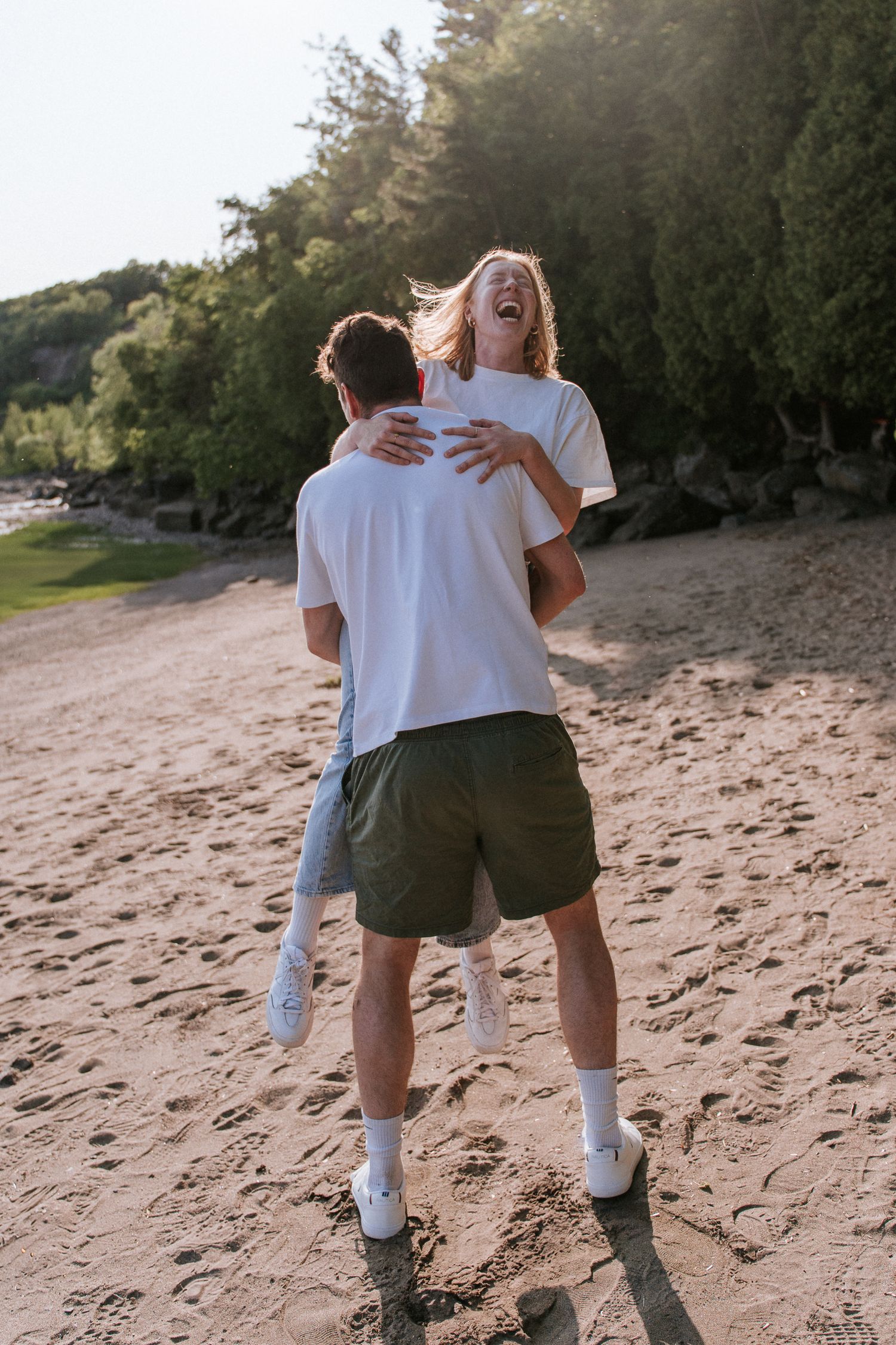 Un couple joyeux vêtu de t-shirts blancs s'amuse sur une plage de sable au coucher du soleil.