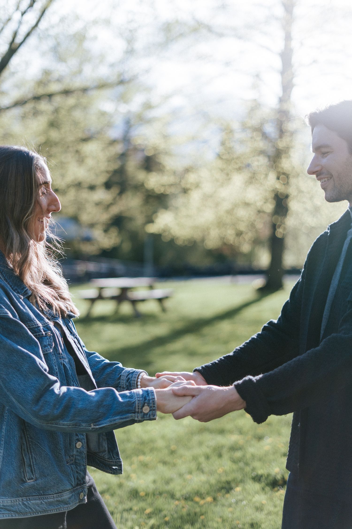 Un couple se tient la main en profitant d'une journée ensoleillée dans un parc, avec des tables à pique-nique et des arbres en arrière-plan.