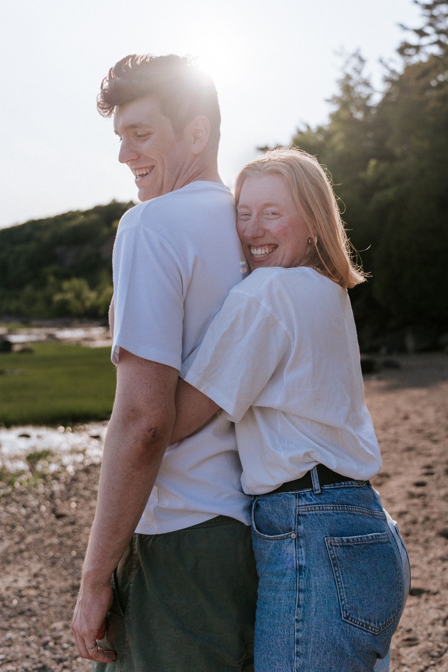Un couple en t-shirts blancs partage un rire spontané au bord de l'eau, au coucher du soleil.