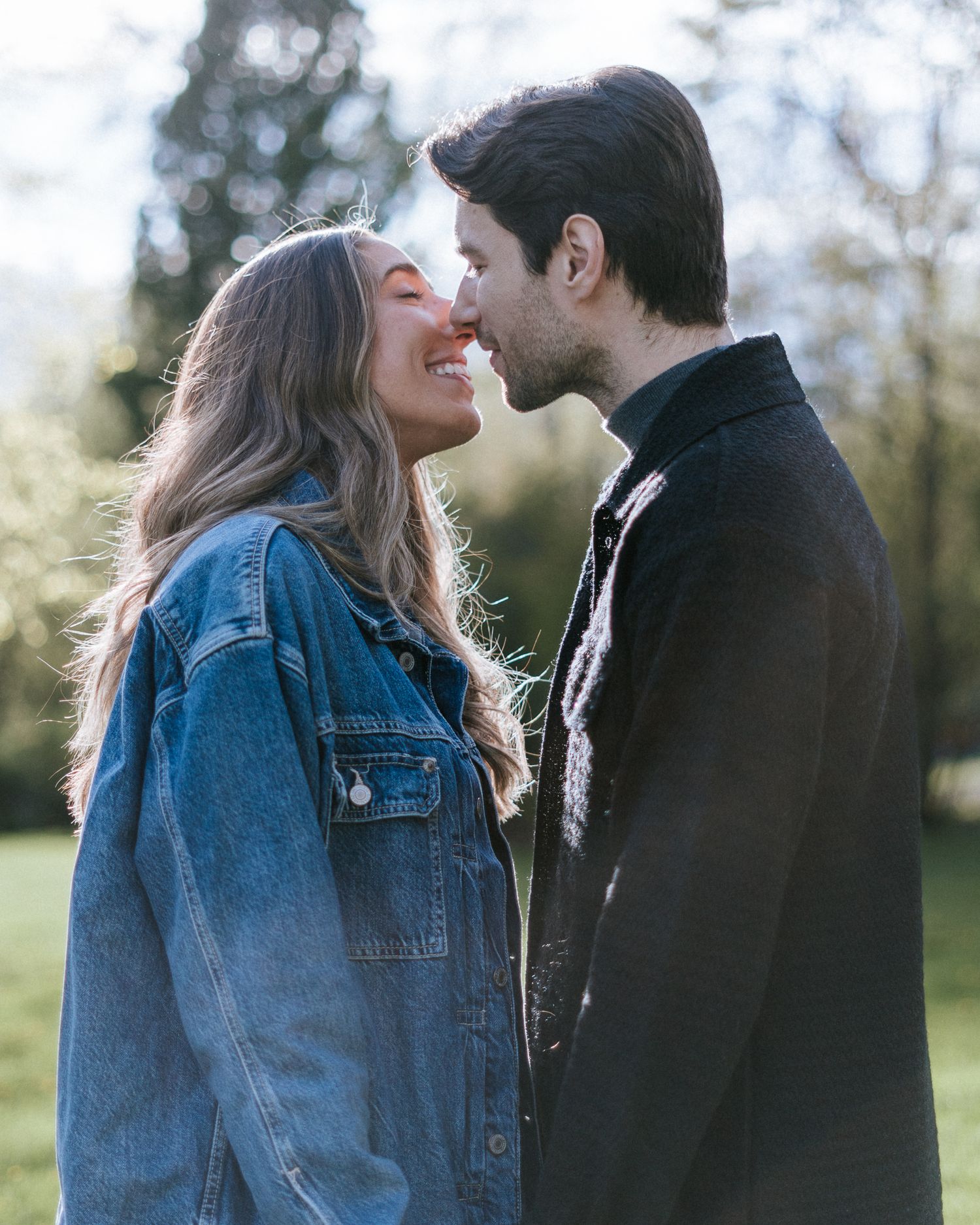 Un couple d'amoureux partage un tendre moment à l'extérieur, la femme en veste de jean et l'homme en veste noire, sur fond de nature.