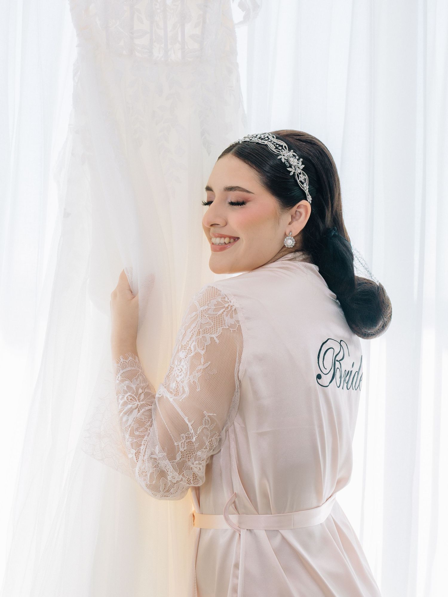 Novia durante el getting ready en el Hotel DoubleTree Mazatlán, abrazando su vestido de boda junto a la ventana