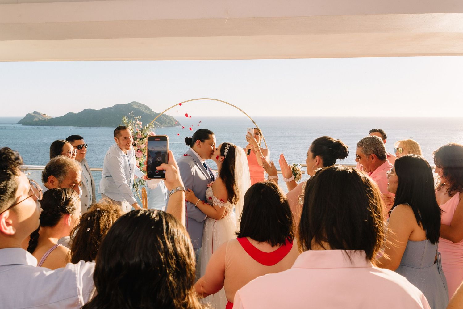 Ceremonia de boda frente al mar en el Hotel Double Tree Mazatlán, pareja de novios besándose rodeados de invitados al atardecer