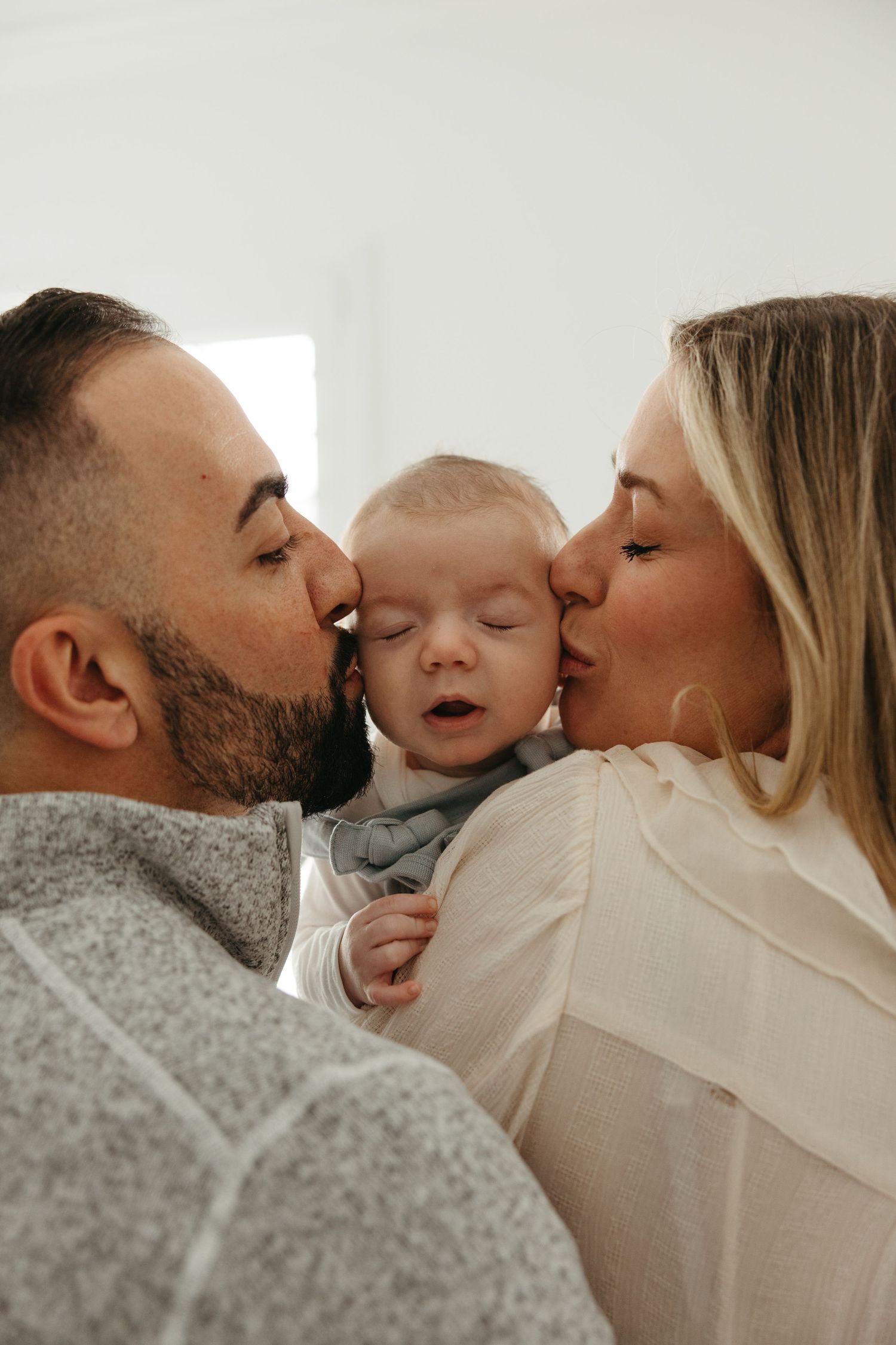 Intimate family moment captured in soft natural light against white background.