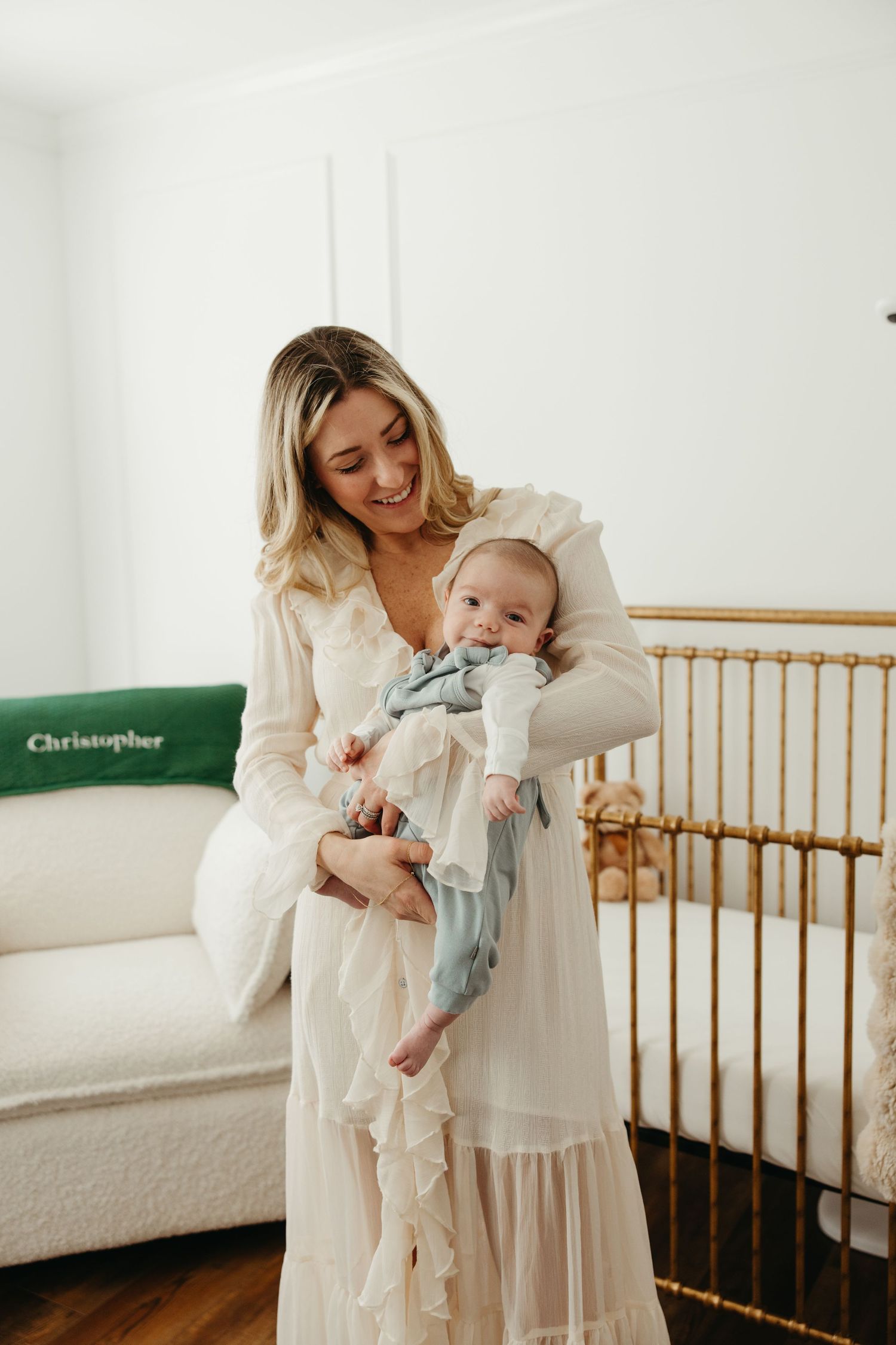 Baby and parent share tender moments in white nursery with wooden crib.