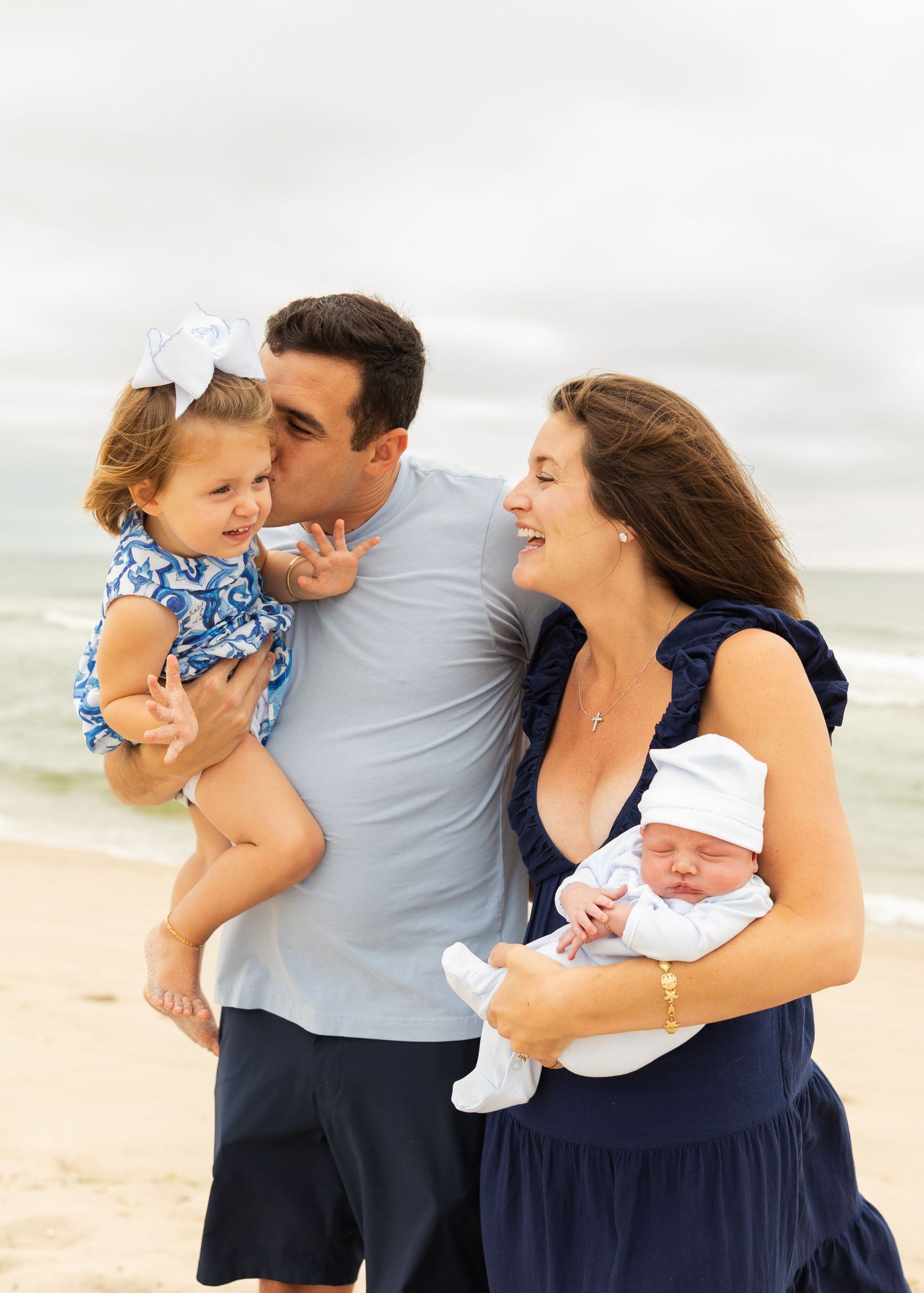 A family of three poses together on a beach wearing coordinating navy and white outfits for a photo session.