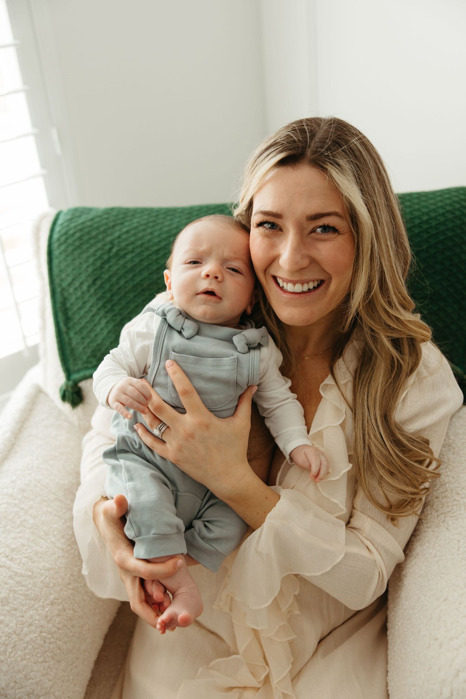A parent and baby share joyful moments on a green couch in a sunlit living room.