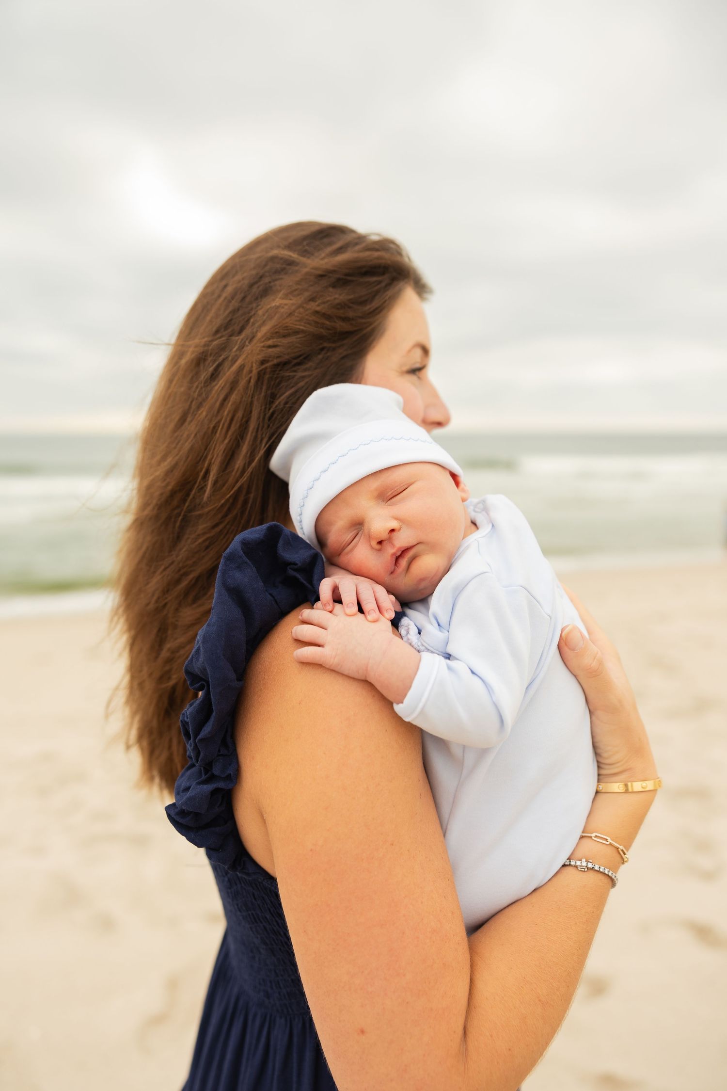 Peaceful moment between parent and sleeping newborn on overcast beach.