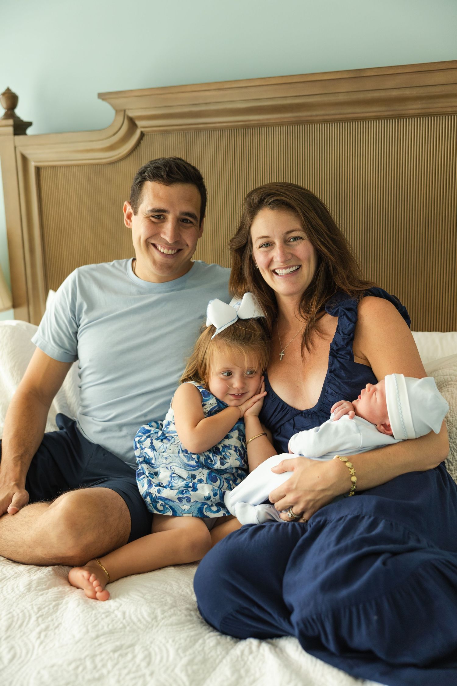 Family lying together on white bedding showing tender moments of connection and joy.