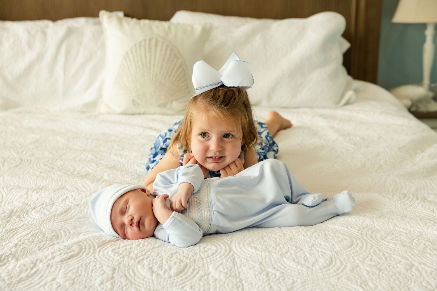 A person wearing light blue clothing lies on white textured bedding in a bright, airy setting.
