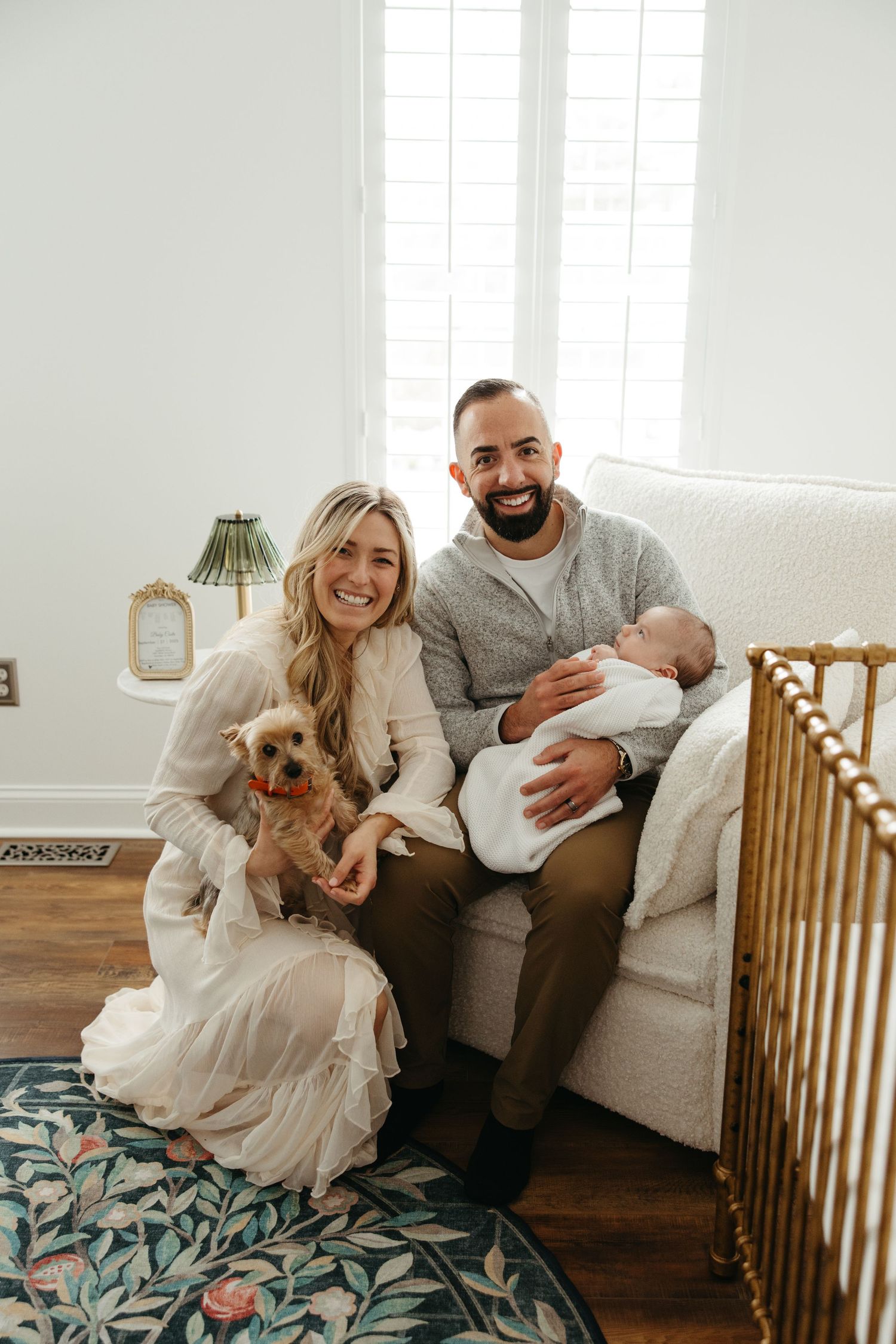 Happy family relaxing in a bright living room with wooden crib and floral rug.