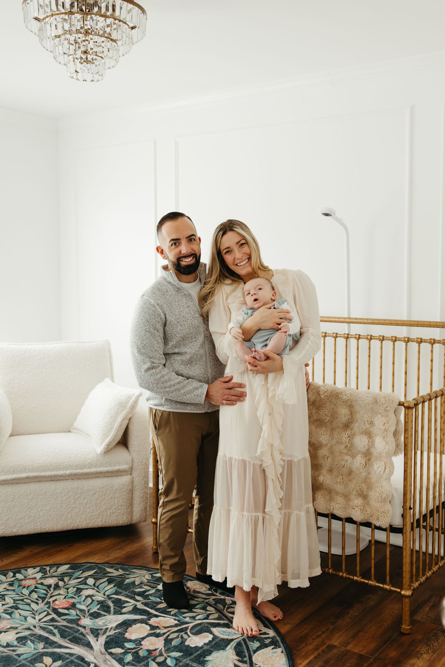 Family poses together in a bright nursery with wooden crib and patterned rug.