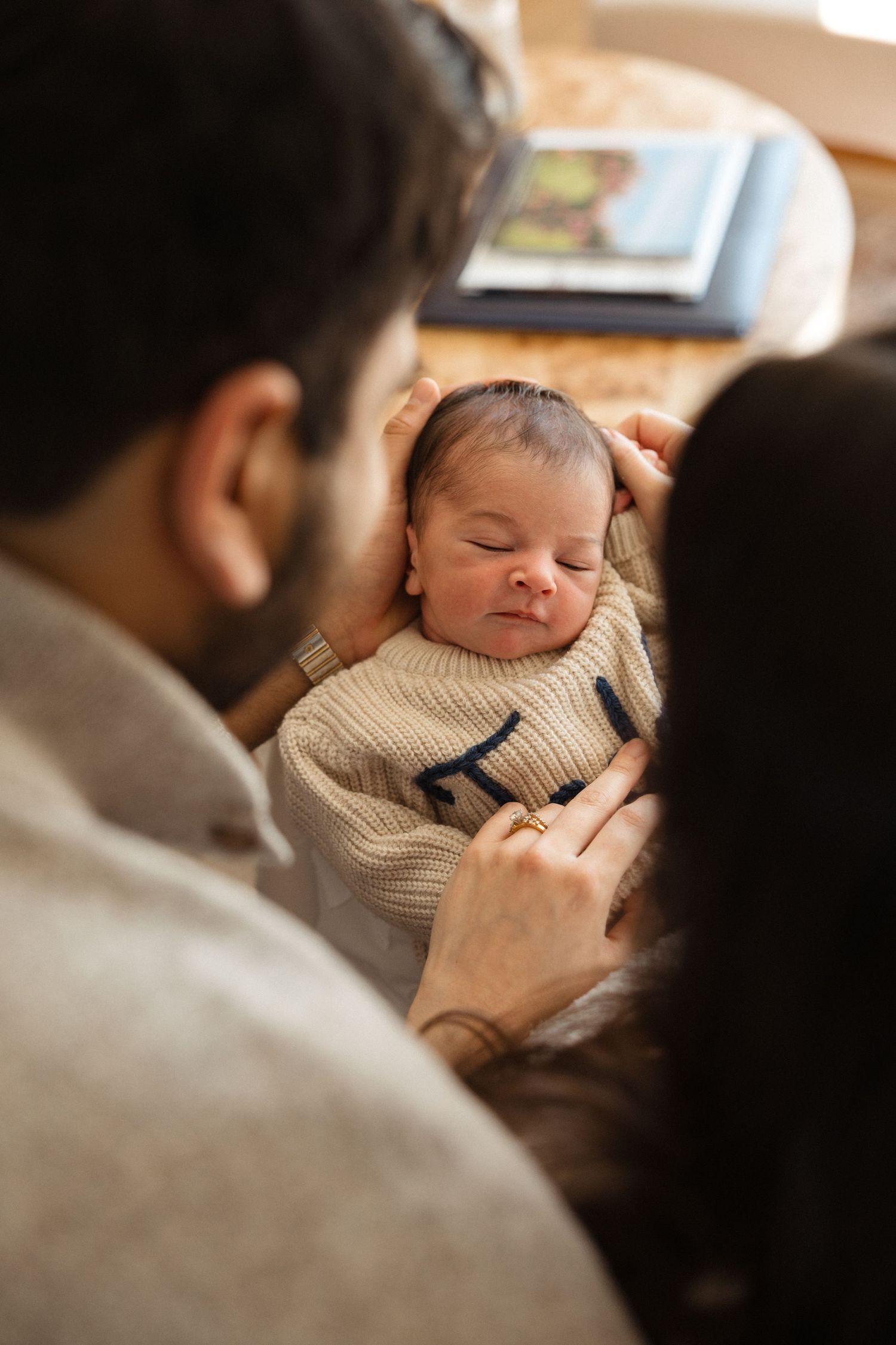 Parents lovingly gazing at their sleeping newborn baby wrapped in a cozy knit blanket.