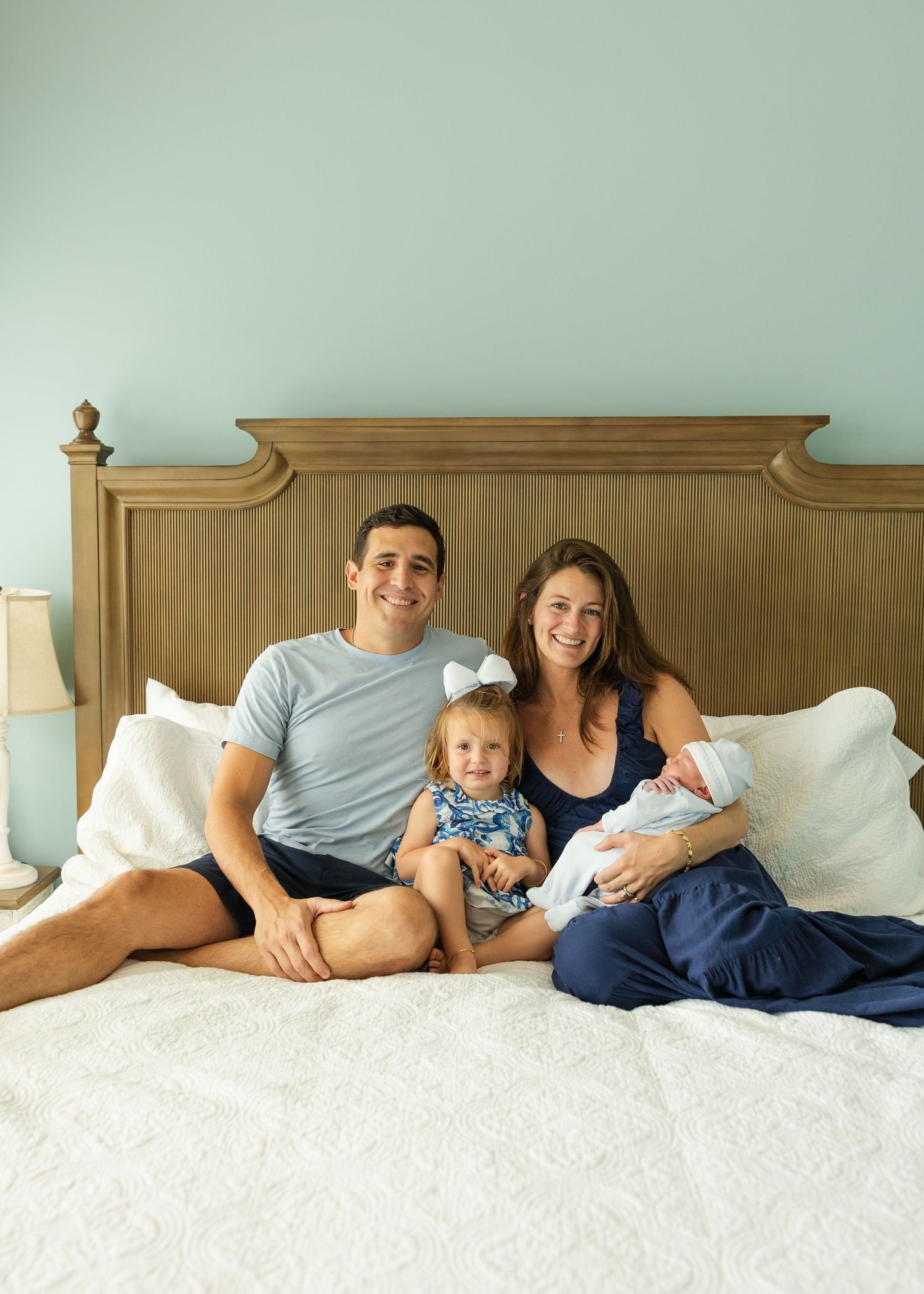 Family relaxing together on a white bed wearing casual clothes.
