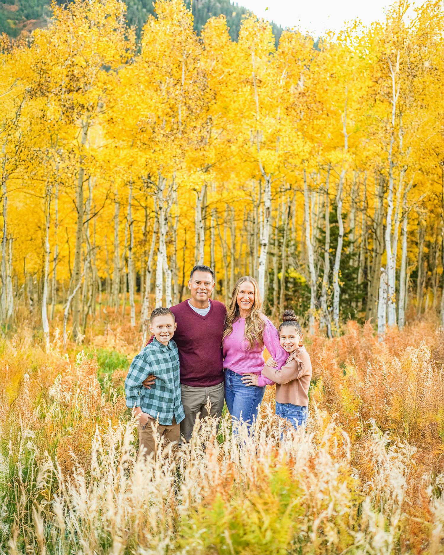 A group enjoying a fall photoshoot among vibrant yellow aspen trees and tall grasses during golden hour.