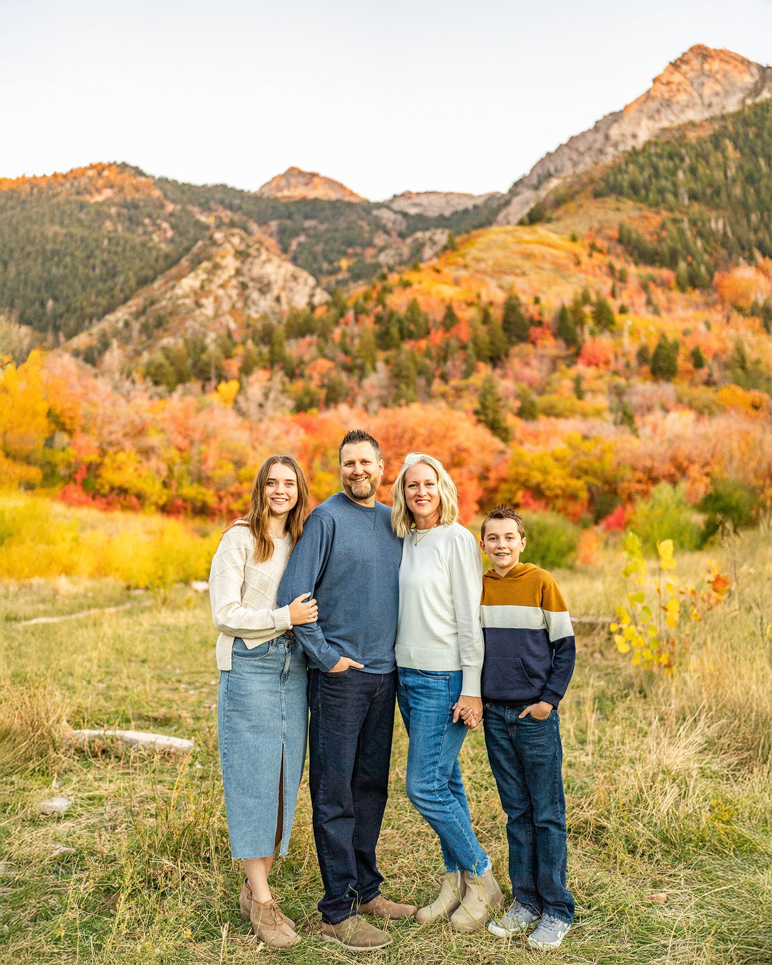 A group stands together against a backdrop of mountains and vibrant autumn foliage in a scenic outdoor setting.