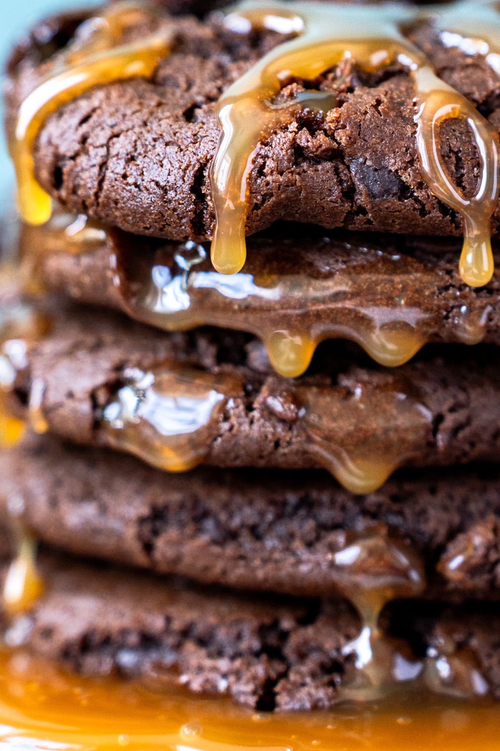 Decadent dark chocolate cookies dripping with golden caramel sauce in a close-up macro shot.
