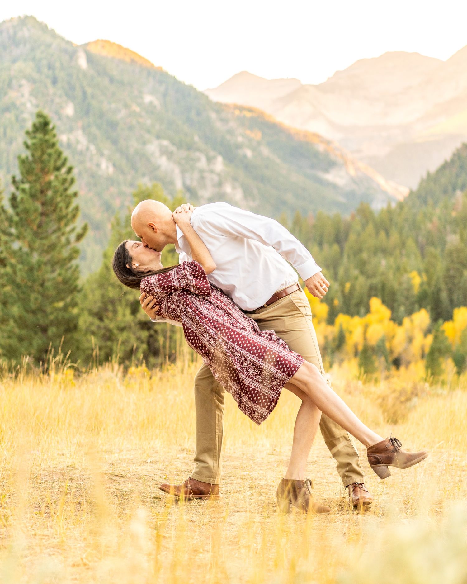 Two dancers striking a pose in a golden field with mountain backdrop during sunset.