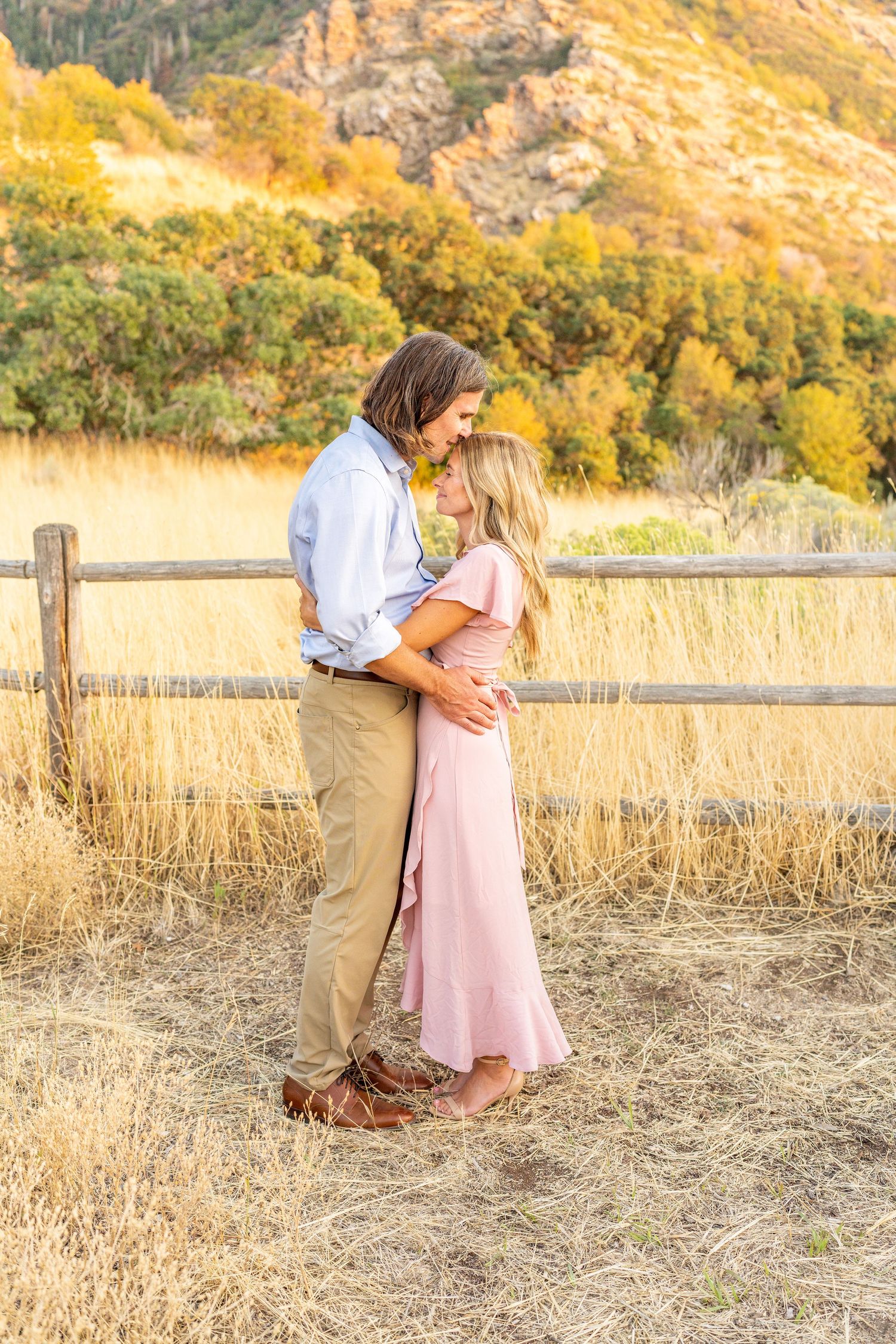 A romantic embrace by a wooden fence with golden autumn mountains and foliage in the background.
