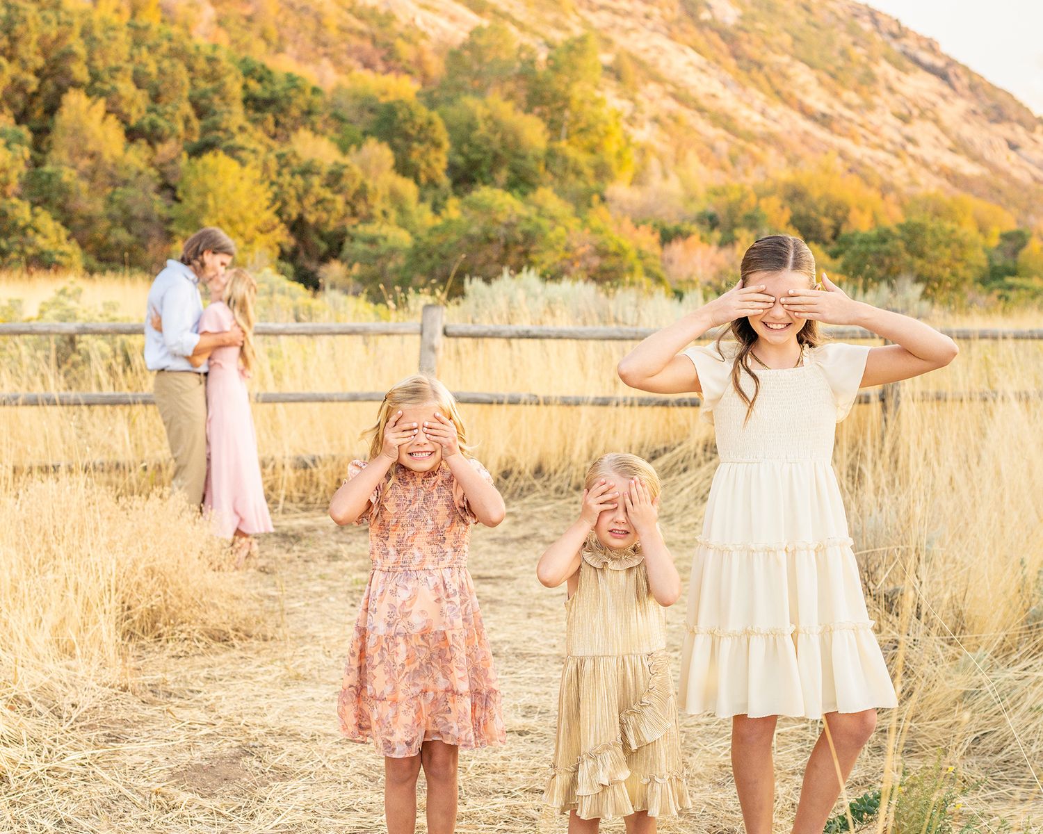 Golden sunlit field with tall dry grass and mountains creates perfect backdrop for outdoor autumn portraits.