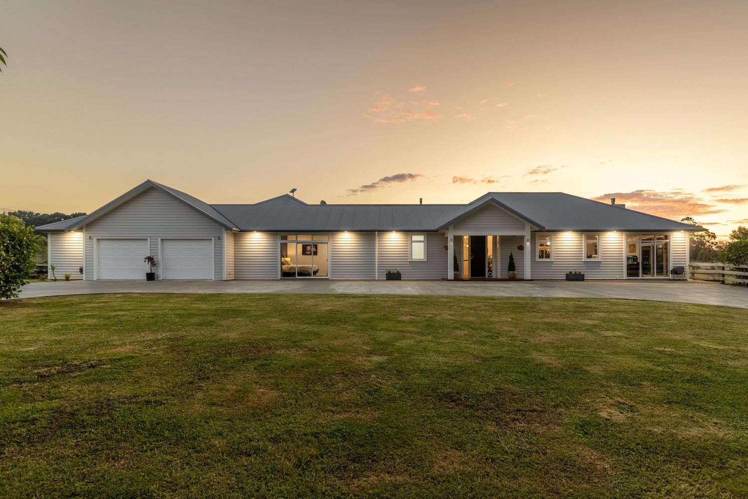 Spacious single-story ranch home with white exterior, triple garage, and manicured lawn photographed at golden sunset.
