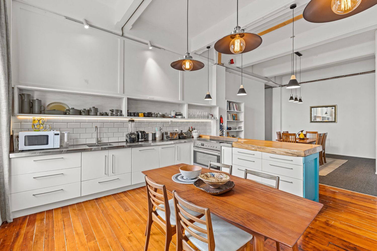 Modern kitchen with white cabinets, wood floors, pendant lights, butcher block island, and dining table in an open-plan loft.