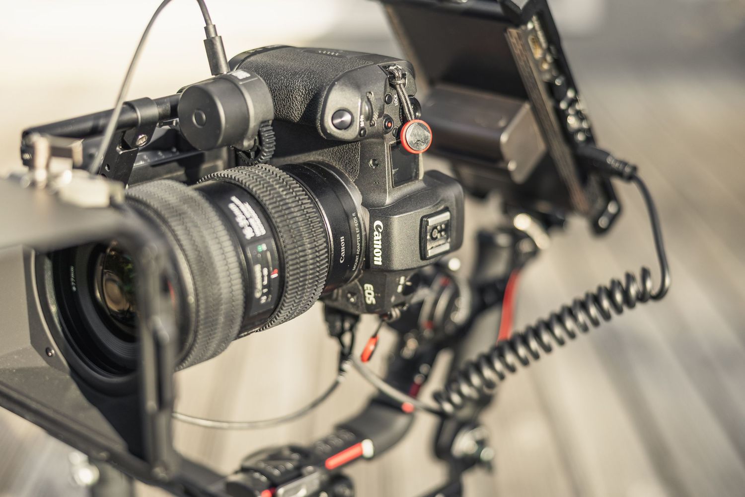Professional camera setup with lens mounted on rig showing coiled cable and stabilization accessories.