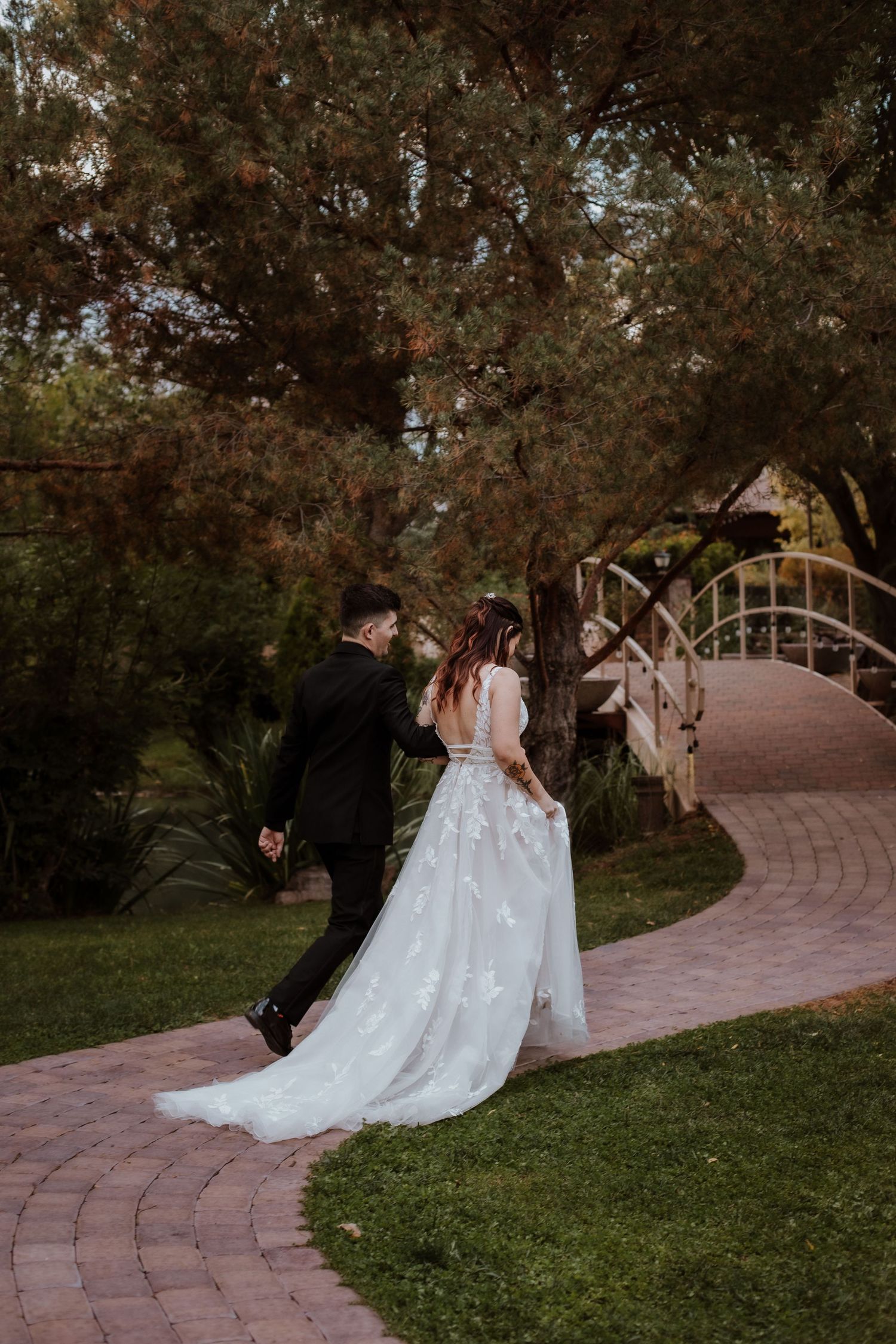 A tender moment at dusk along a curved brick pathway between an elegant white wedding dress and dark suit. Benson weddding photographer