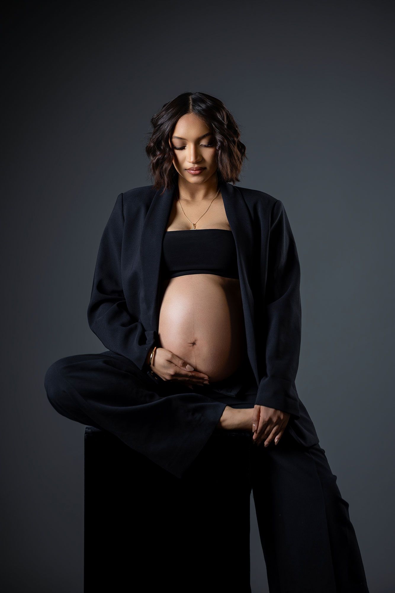 Dramatic maternity portraits in black outfit against dark background highlighting the pregnant form.