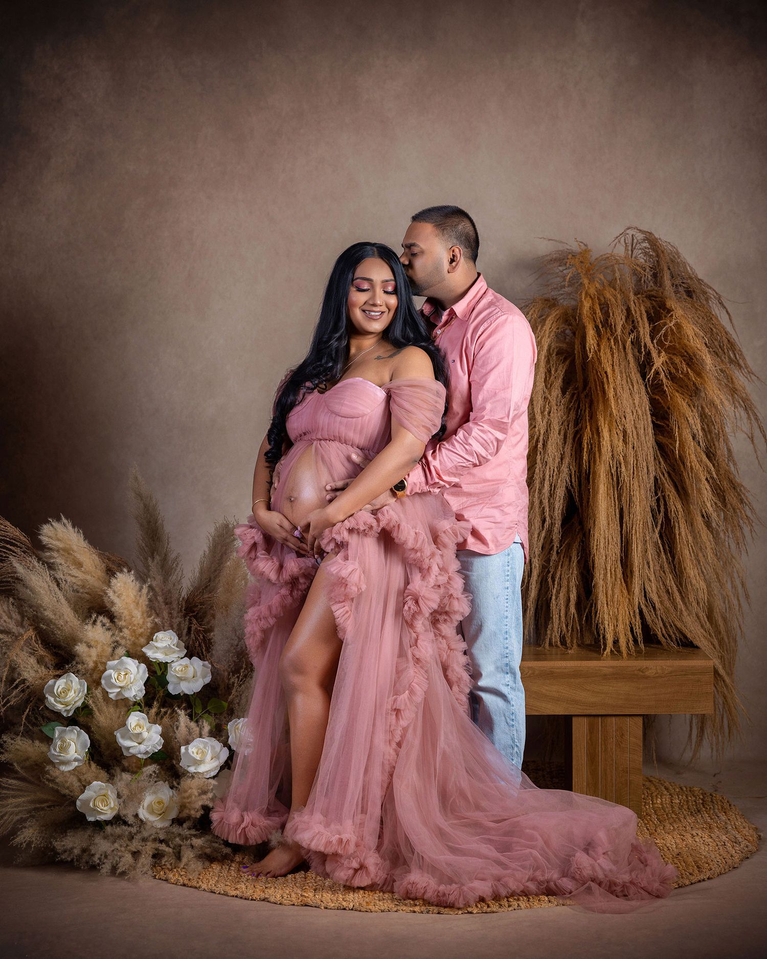 A romantic maternity photoshoot featuring a couple in pink and white with rustic decor and floral elements.