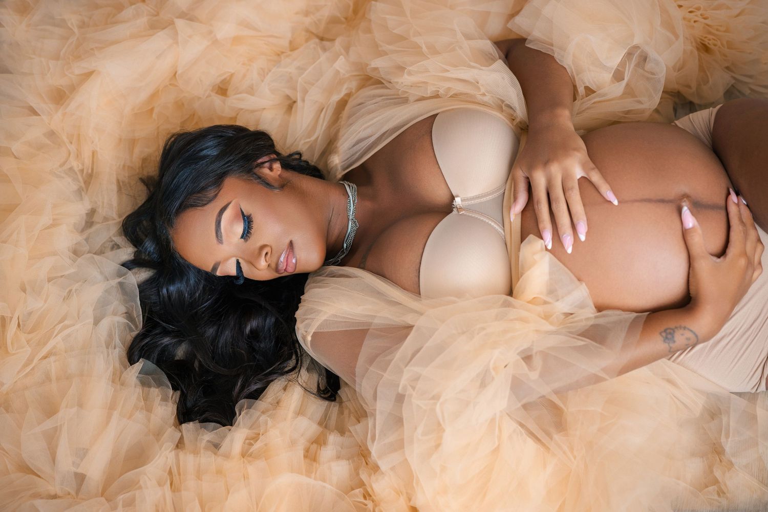 Artistic maternity photo with flowing champagne tulle fabric and soft lighting creating an ethereal mood.